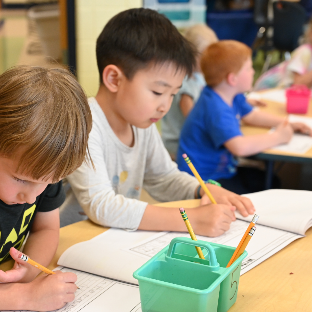 A group of students writing on paper at the table focused on their work