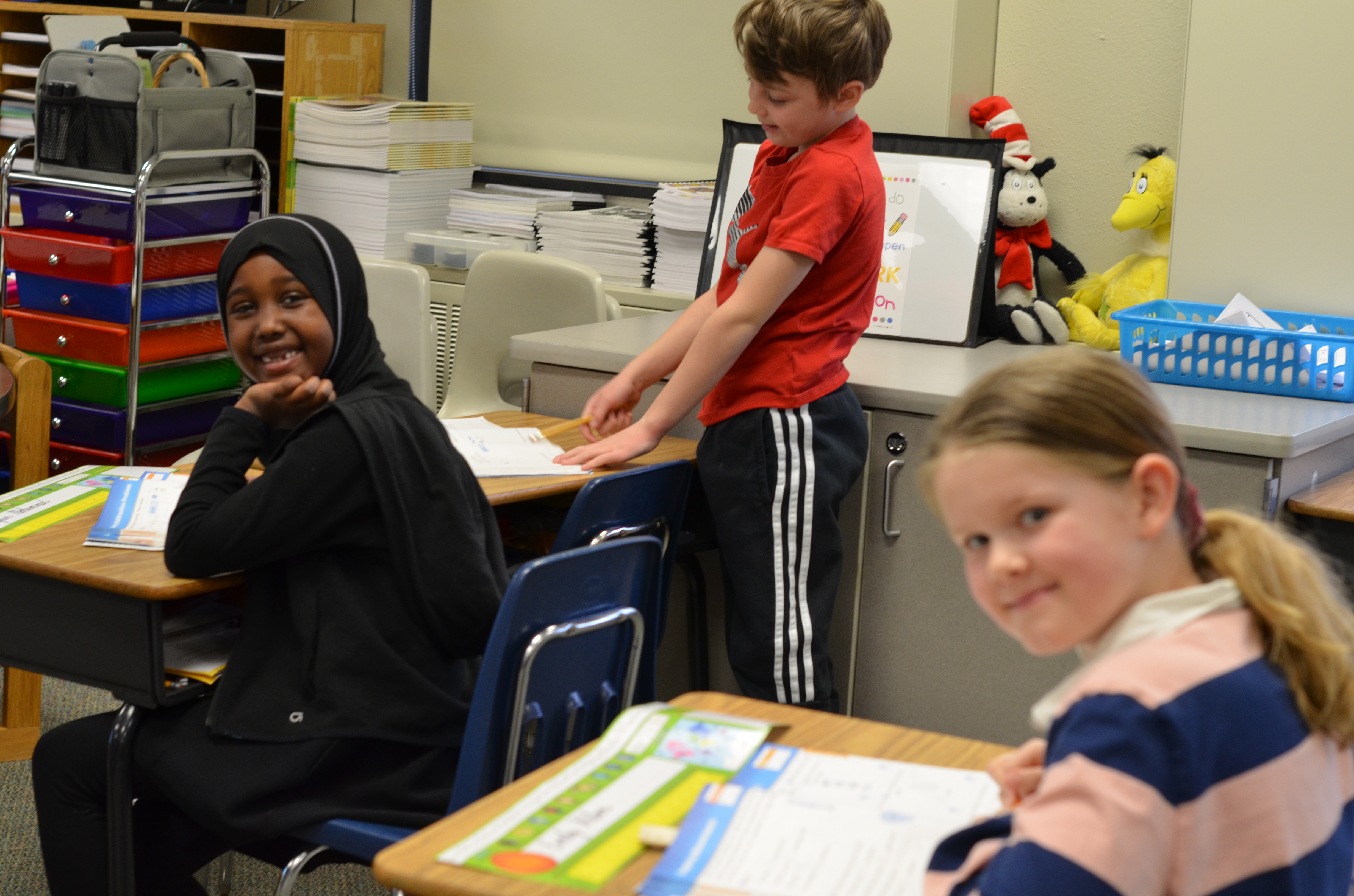 students sitting at desks, smiling at camera