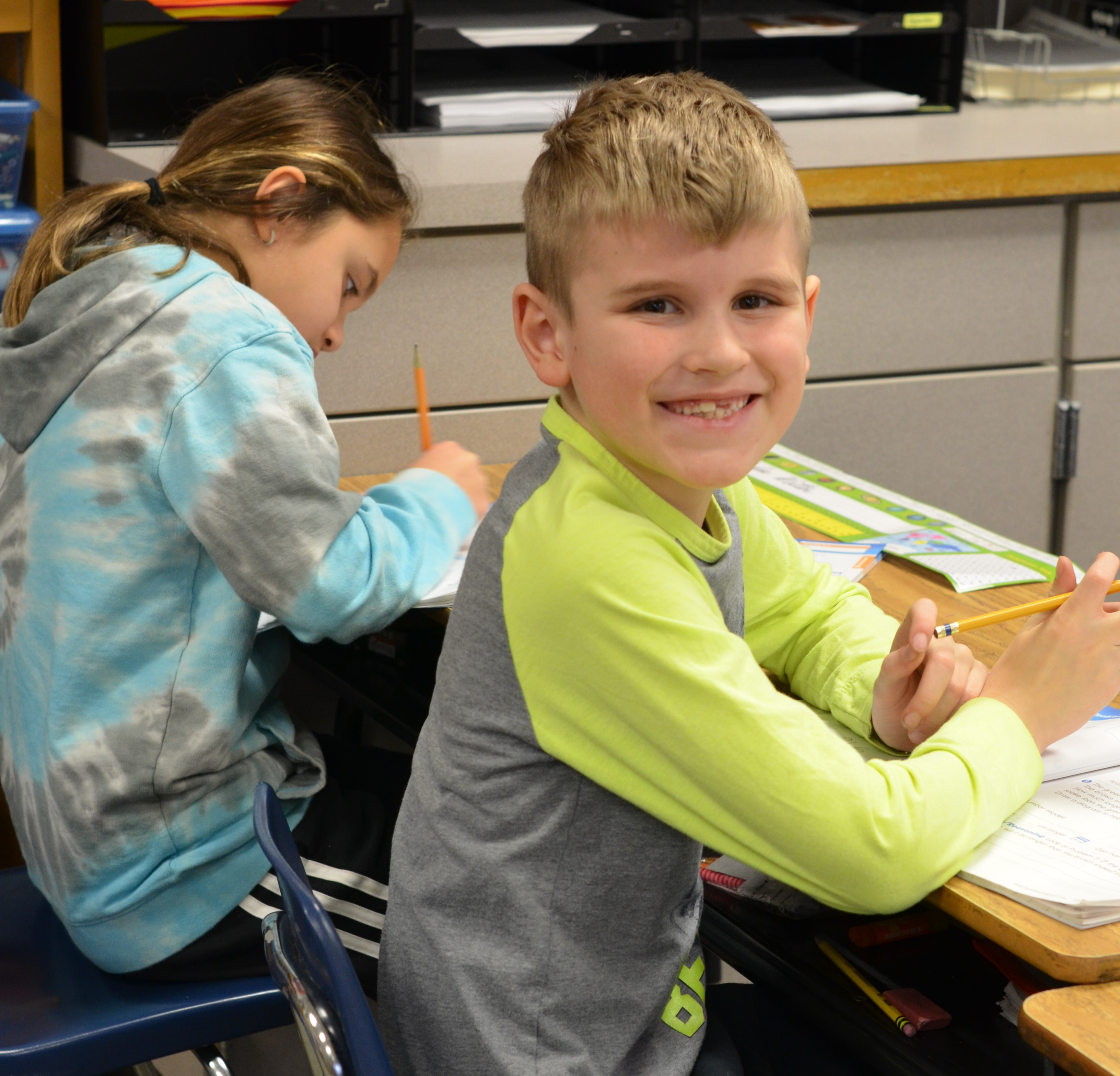 young male student sitting at desk, smiling at camera