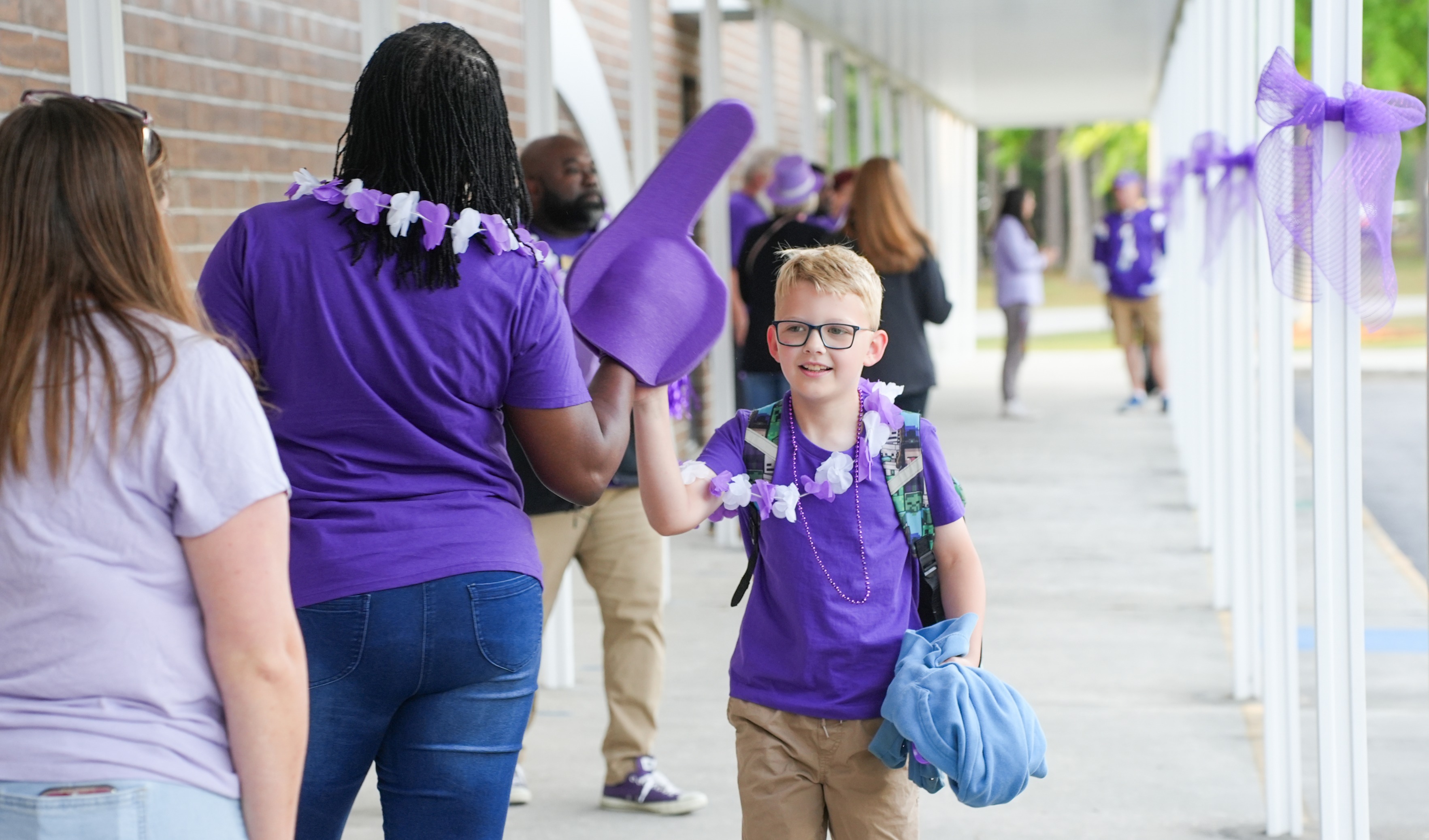A group of adults and a child in purple wear standing under a corridor with purple ribbons.