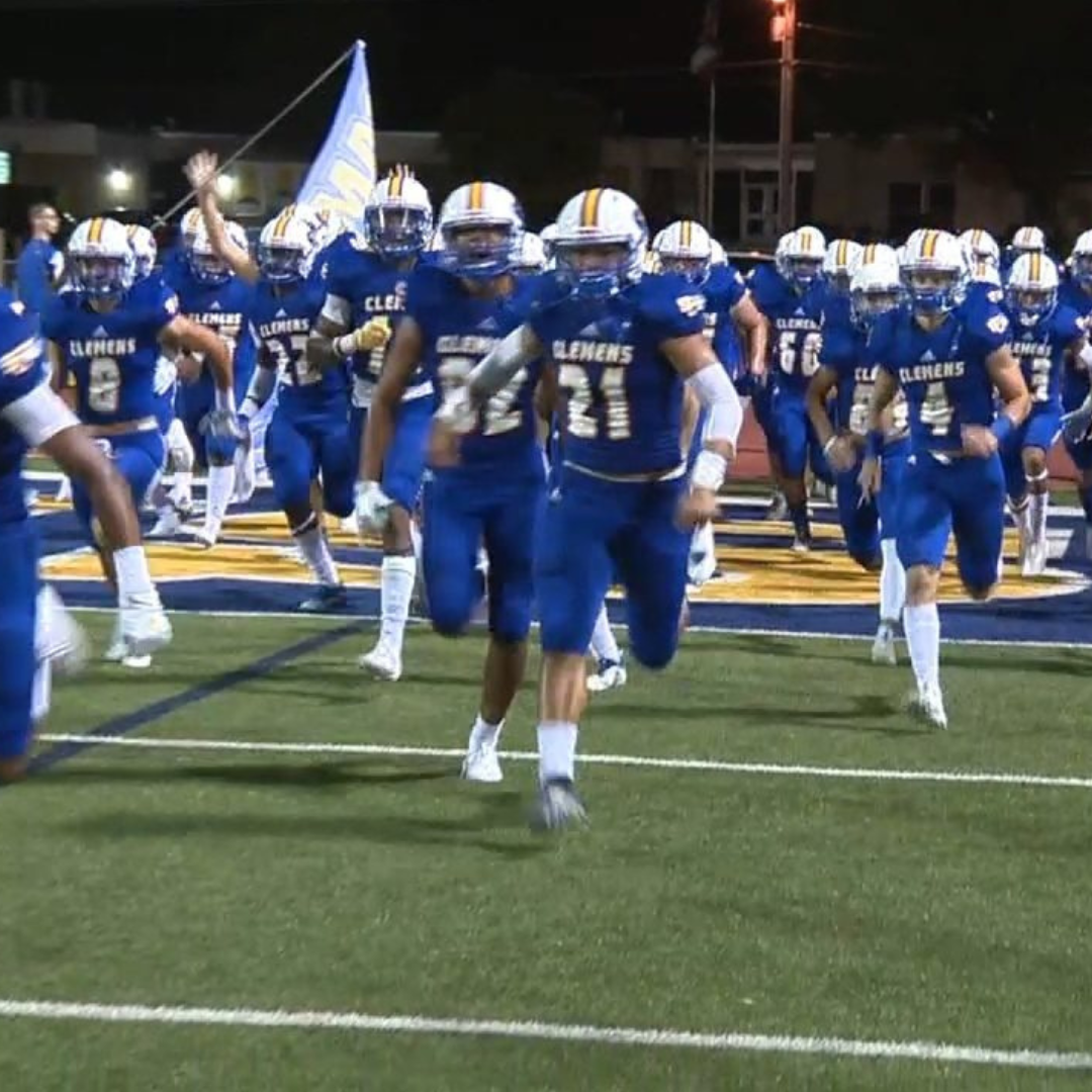 samuel clemens football team in blue uniforms charging towards camera across football field in blue & white uniforms