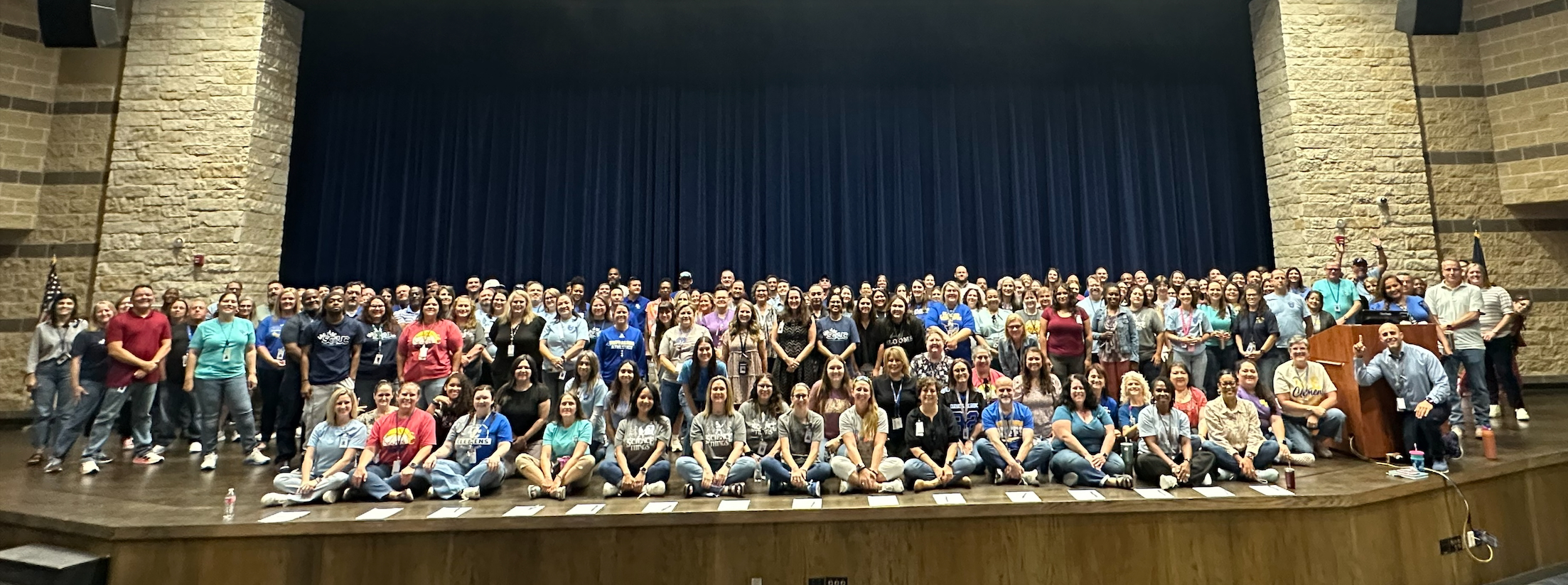 clemens faculty spread sits & stands across the stage in the auditorium of the performing arts center