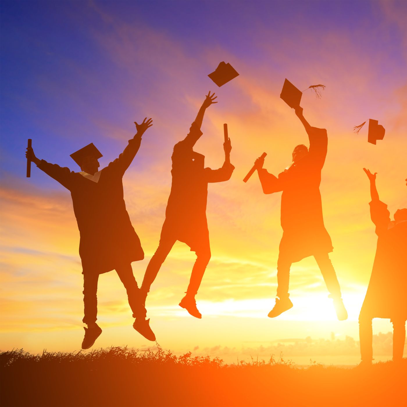 Silhouette of graduates jumping with a sun background
