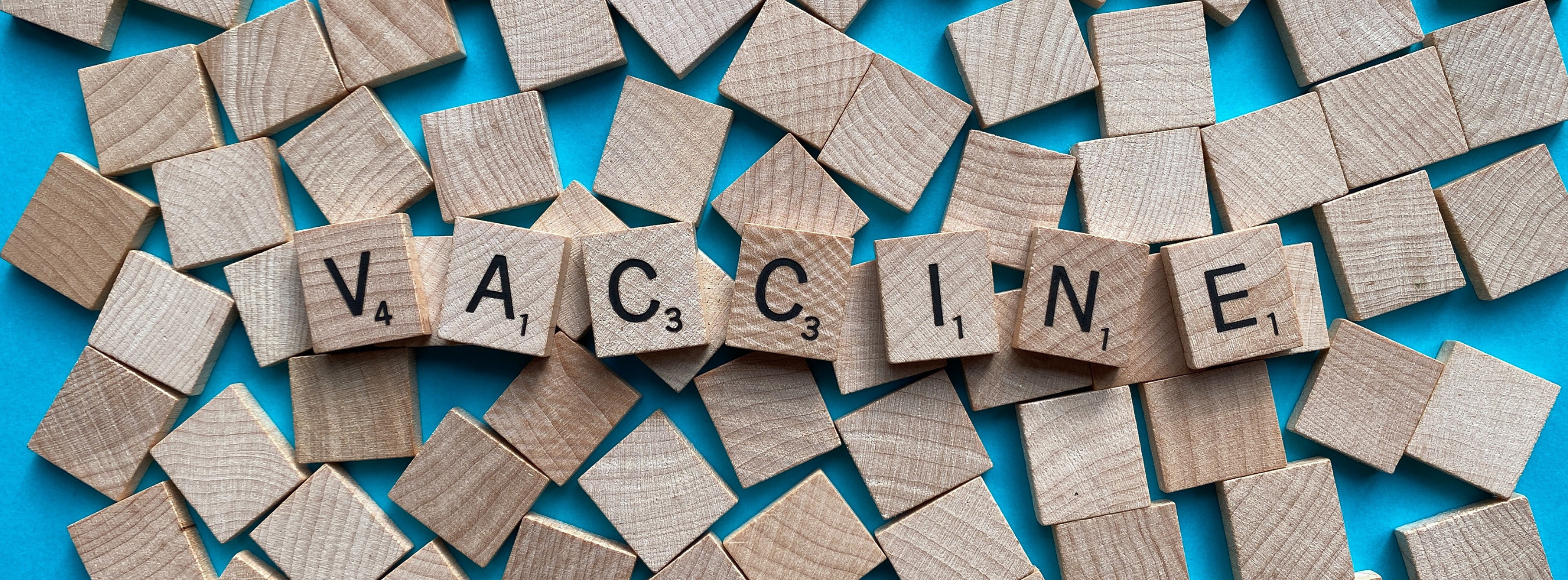 The word "Vaccine" spelled out on Scrabble tiles on a blue background
