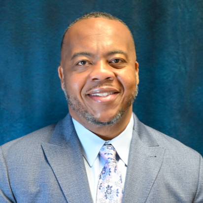 Man with short hair, smiling, wearing a gray suit and a blue tie with white patterns.