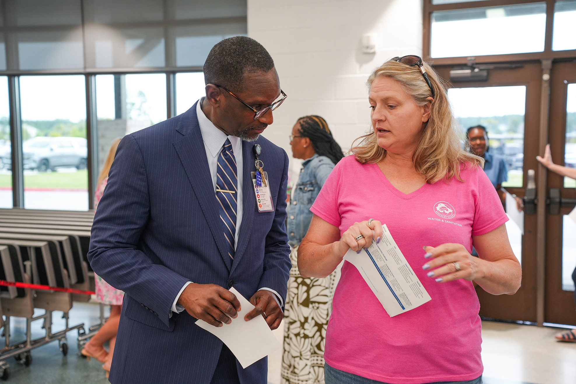 Man and woman reviewing documents. Woman wearing a pink shirt. Man in a blue suit and tie.