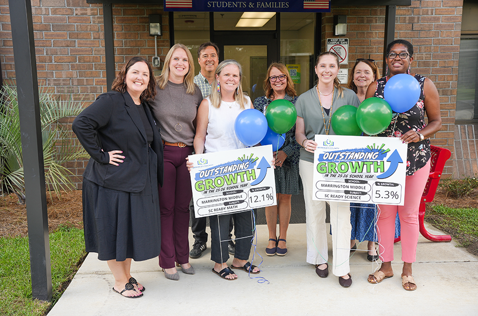 Group of women holding signs with numbers and balloons in front of a building.