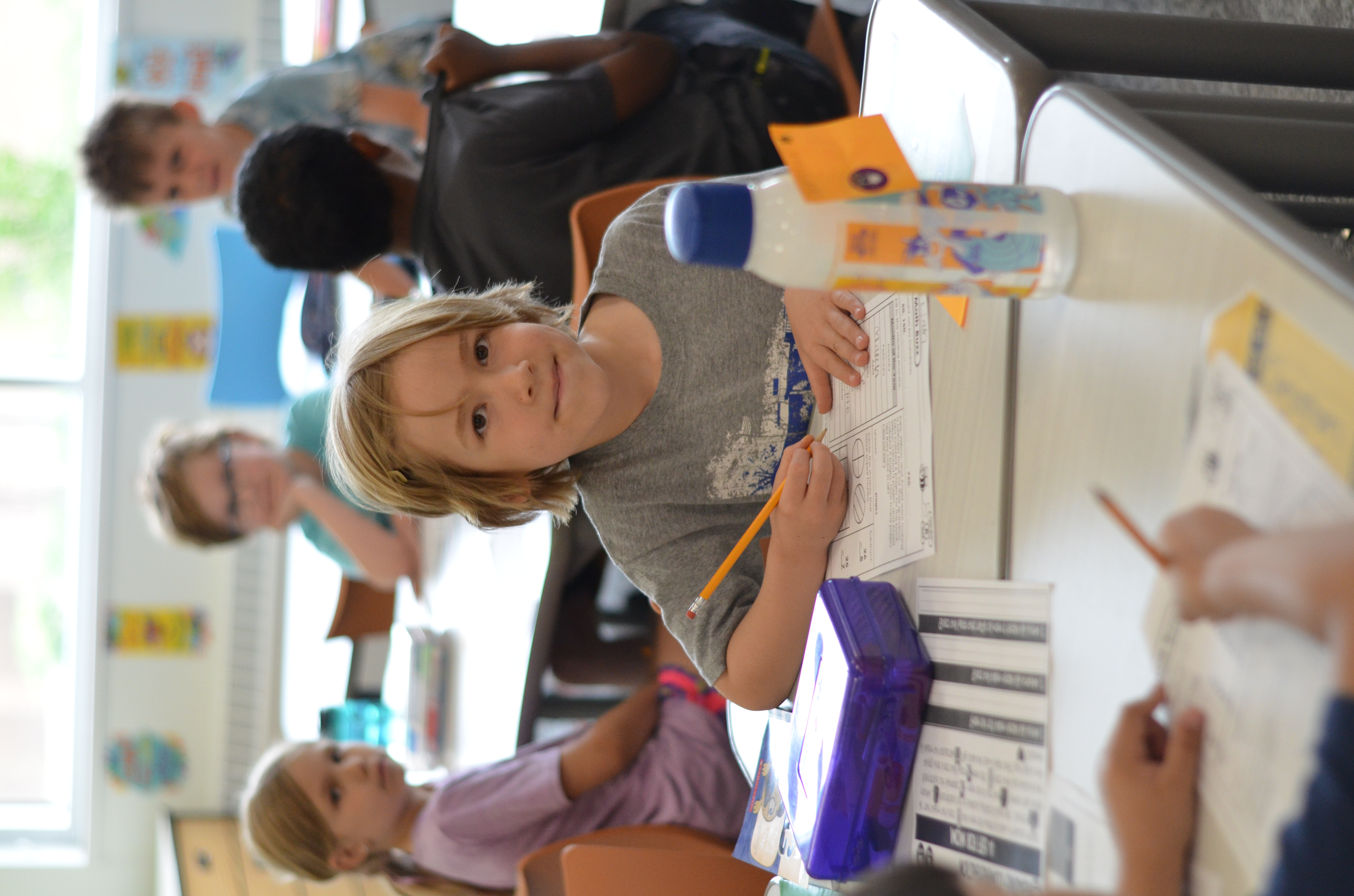 young girl smiling at camera while writing on paper at desk
