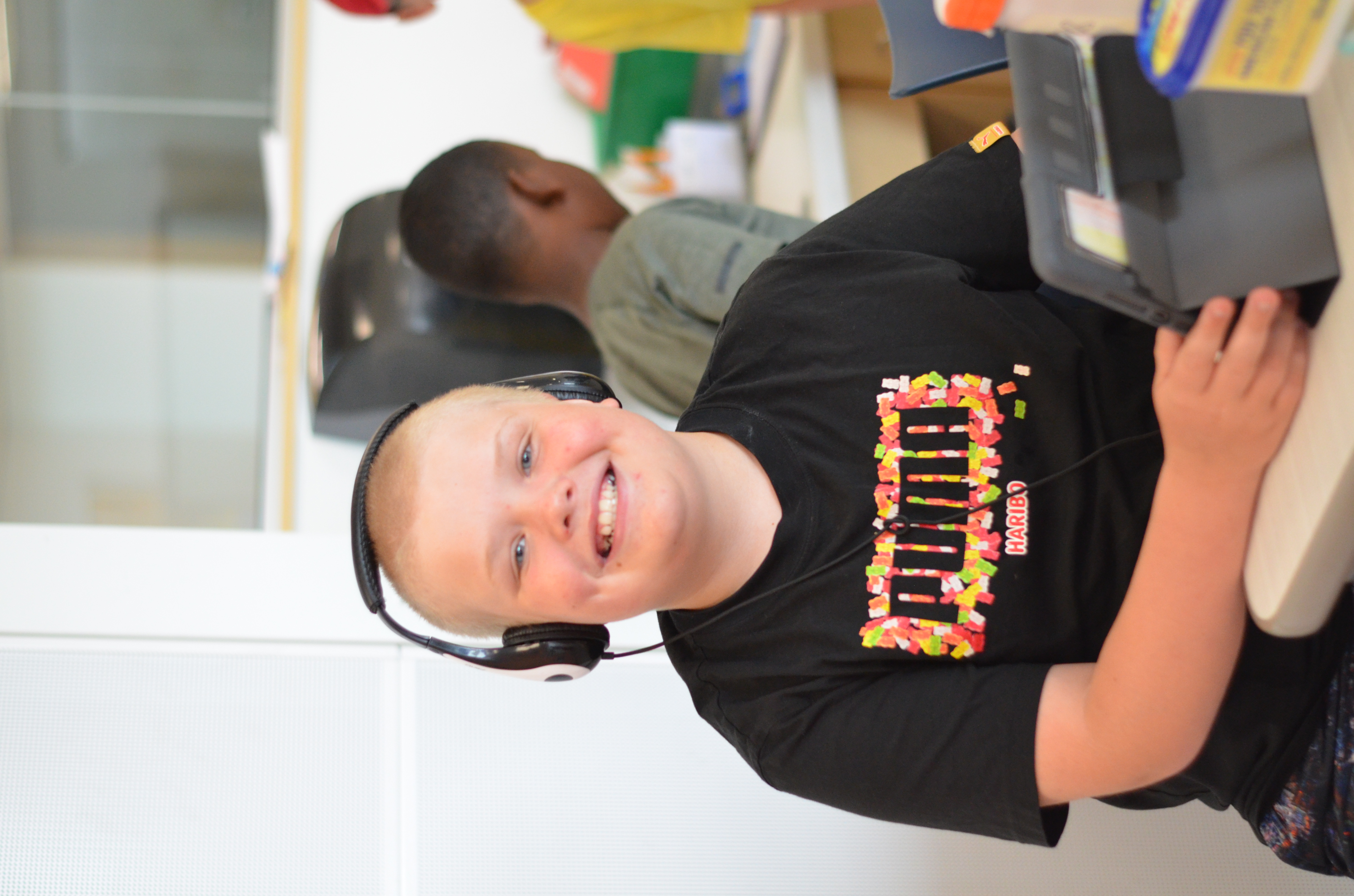 young boy on ipad with headphones smiling at camera