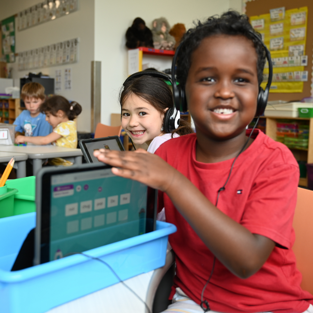 two students working on a listening project with headphones on smiling at the camera