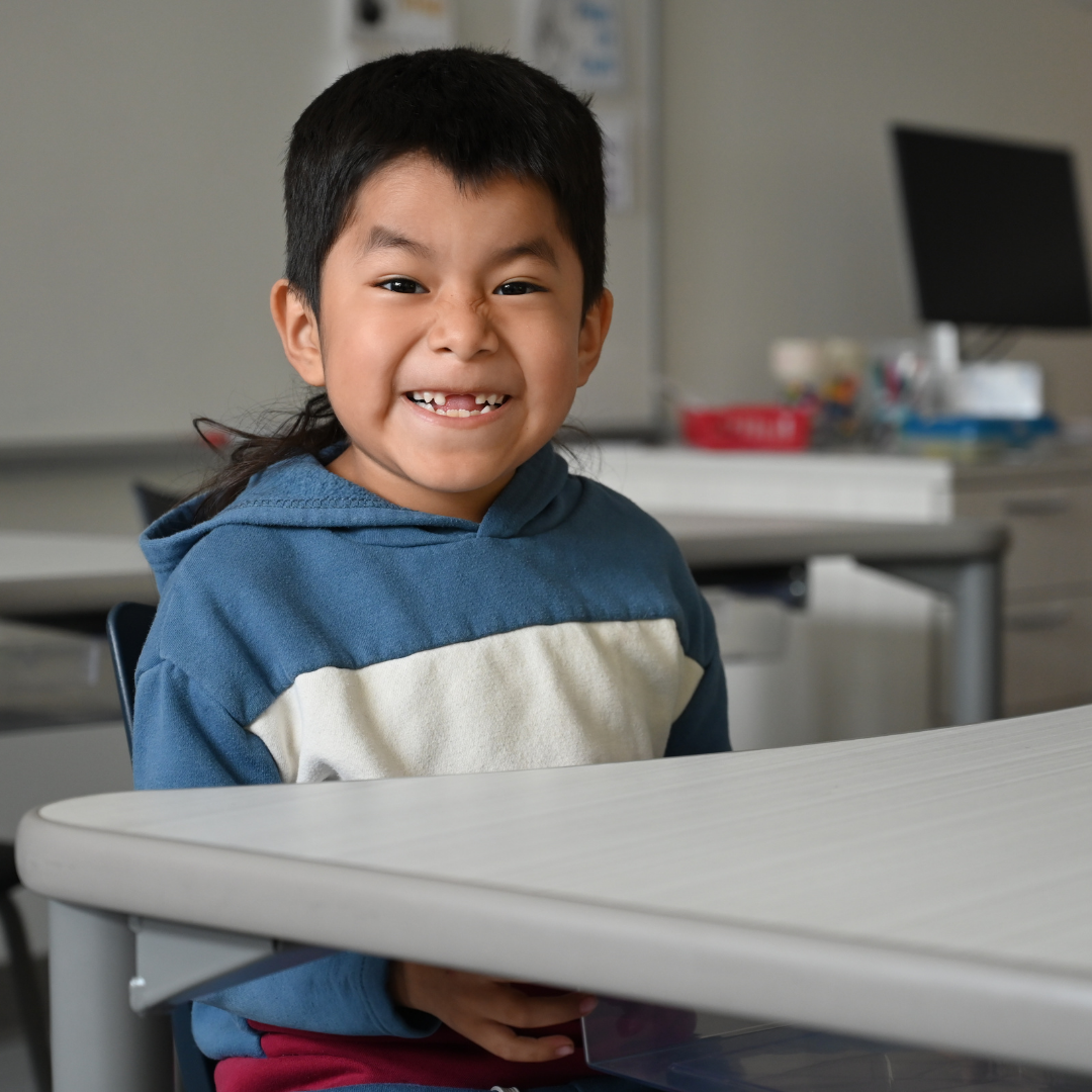 student sitting at table smiling at the camera