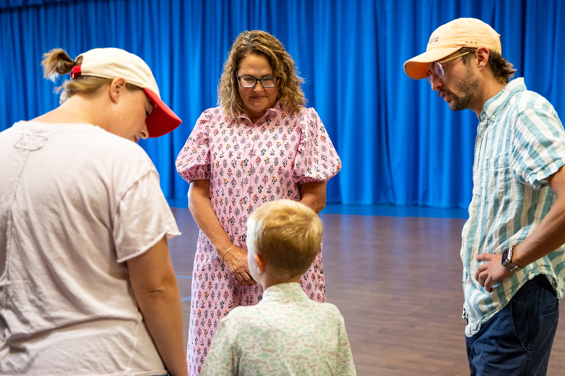 Four people, including a child, stand in a theater. One wears glasses, and another wears a cap.