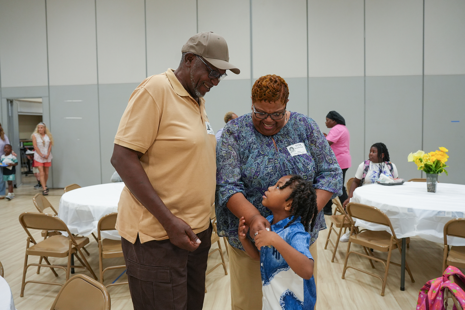 Man and woman holding hands with a child in a large room with tables and chairs.