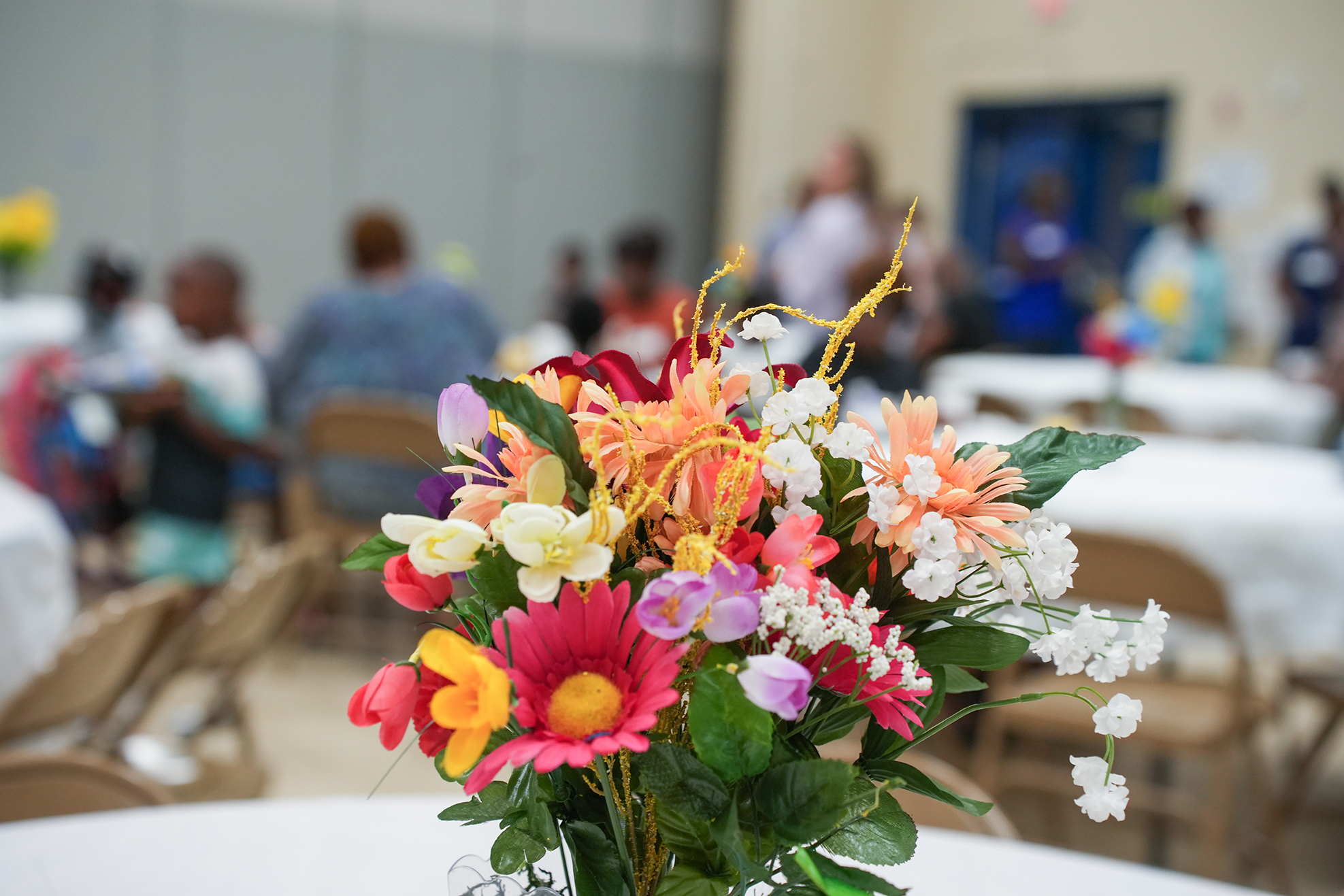 A vase of colorful flowers on a table in a room with chairs and tables in the background.