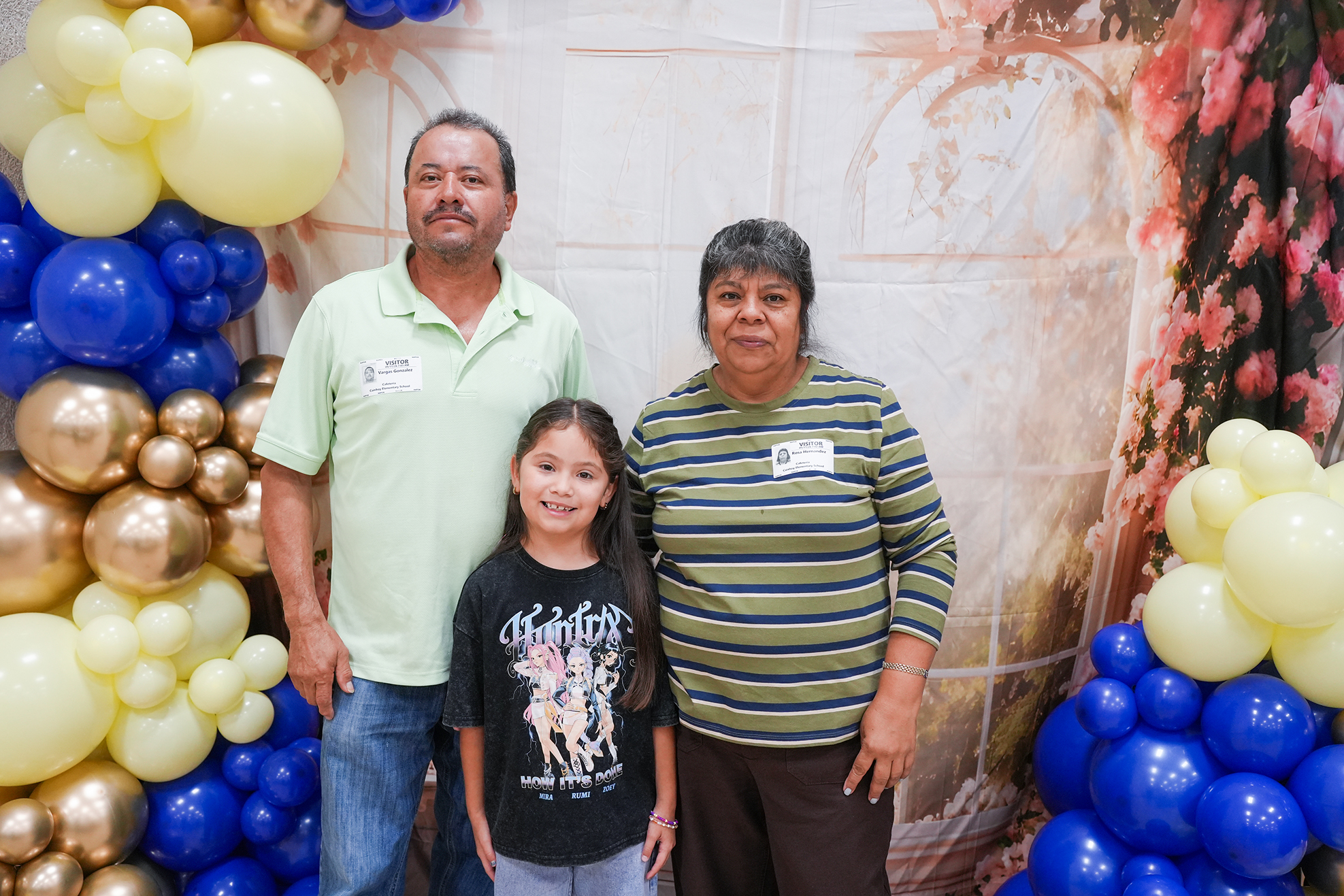 Adult man and woman with young girl standing by a balloon arch. They are looking at the camera.