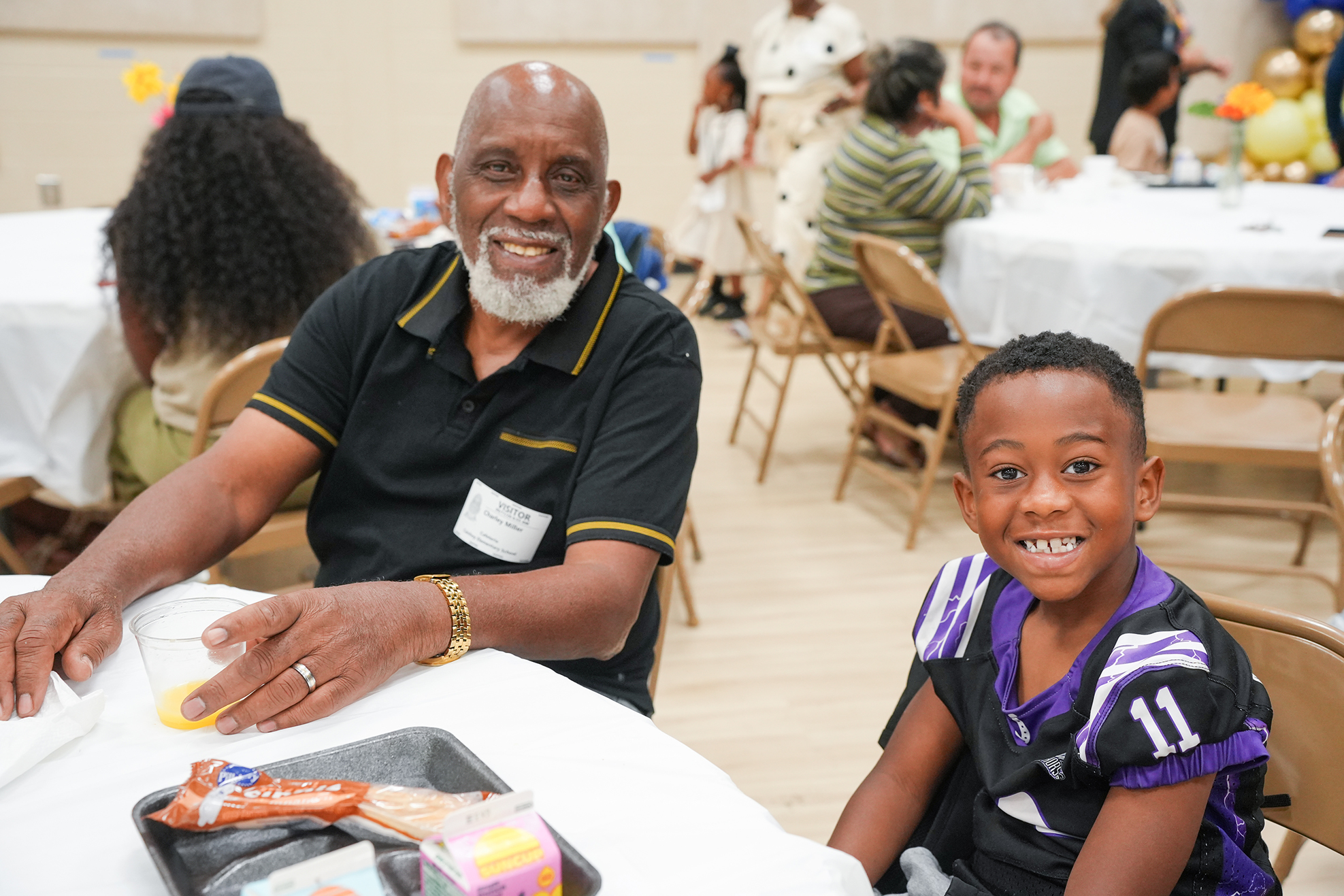 Man and boy sitting at a table in a dining hall. Other people are seated at tables.