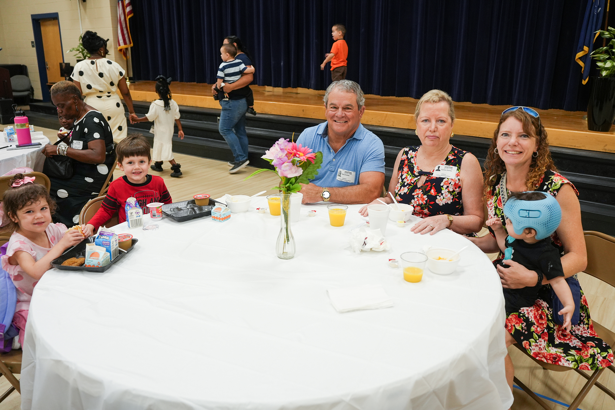 A group of people, including adults and children, sit around a round table in a room.