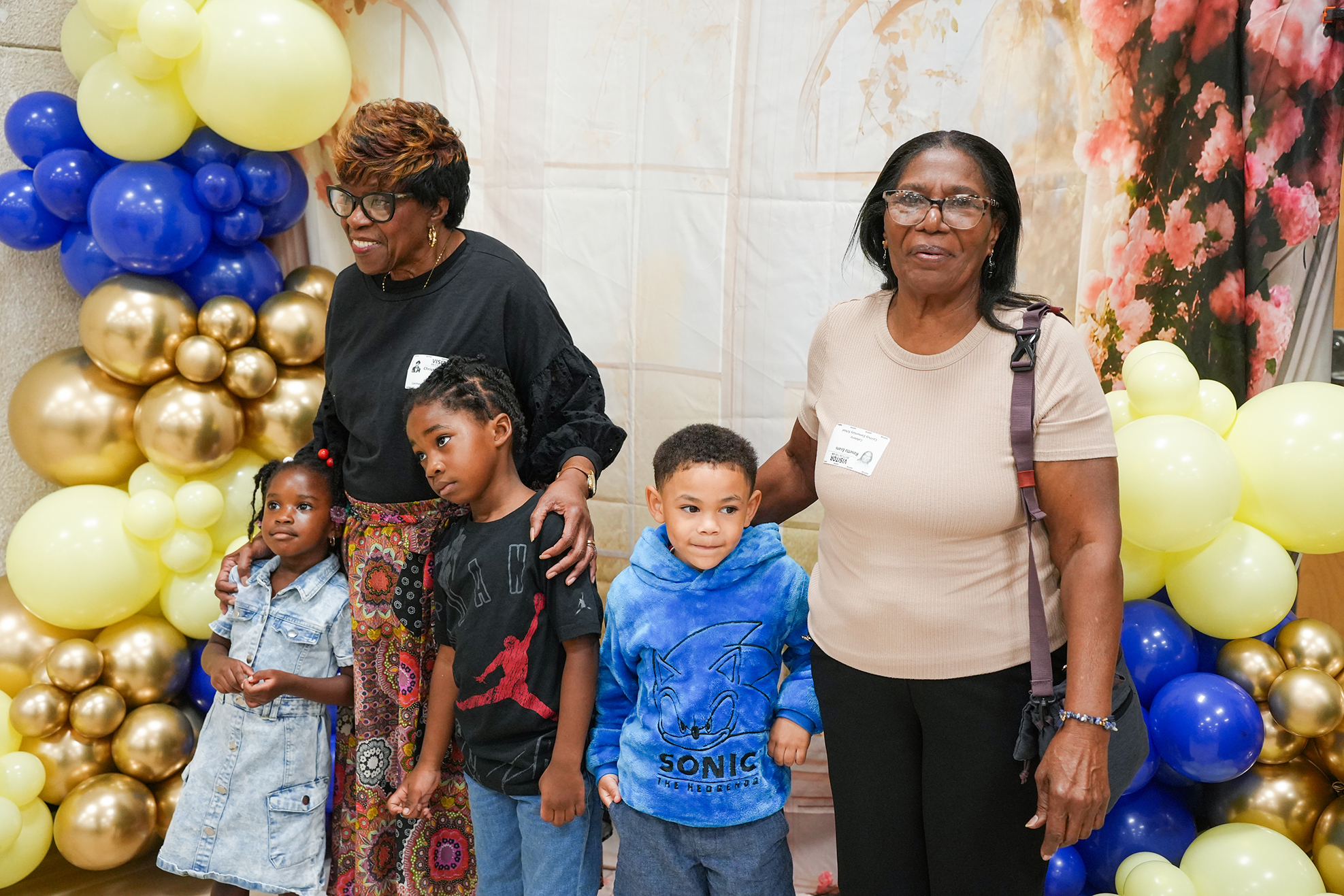 A family of five standing next to each other with colorful balloon decor in the background.