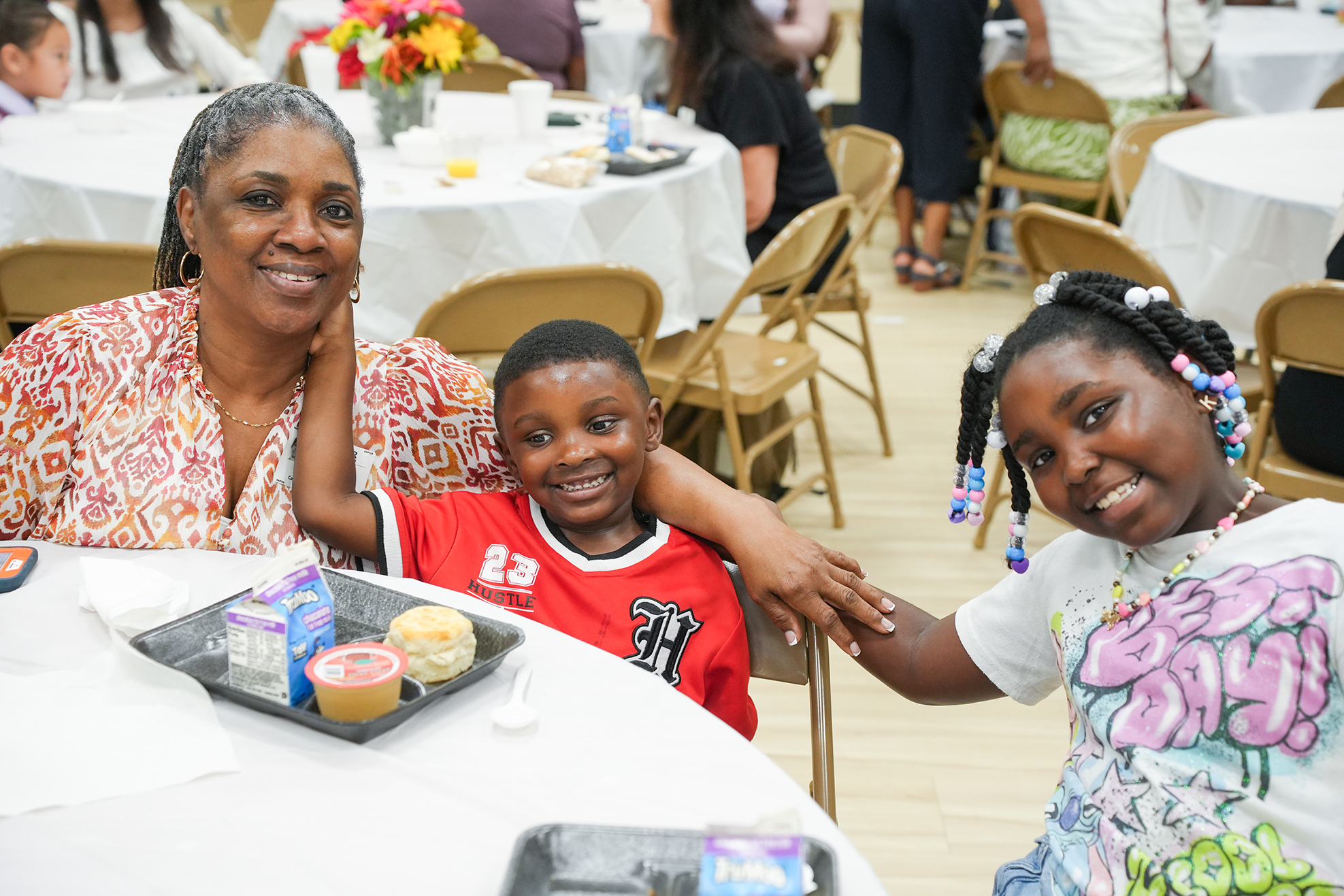 A woman and two children at a table, smiling and posing for a photo. A tray of desserts is on the table.