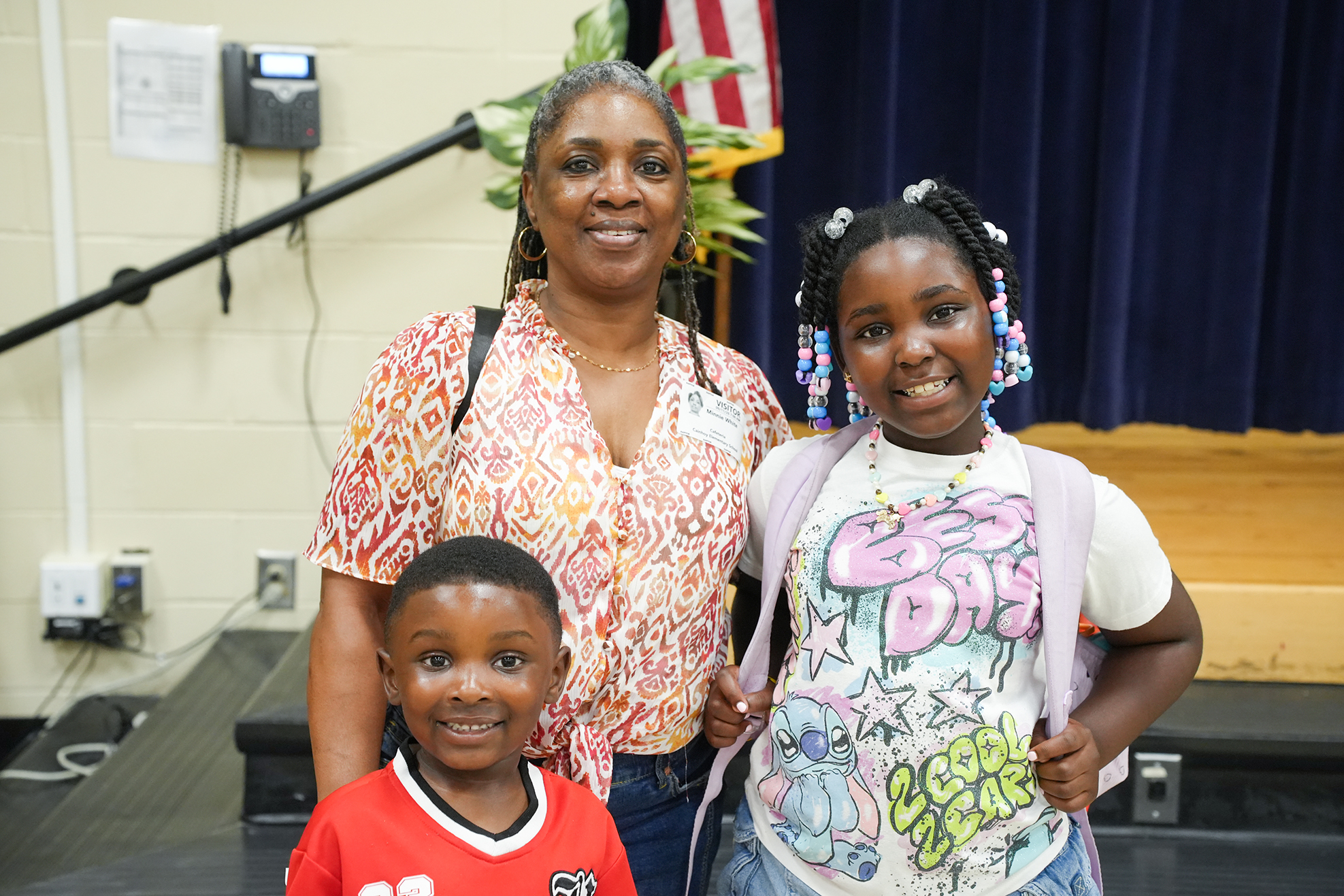 Two children and a woman stand together. The woman is smiling and the children are smiling. A stage is behind them.