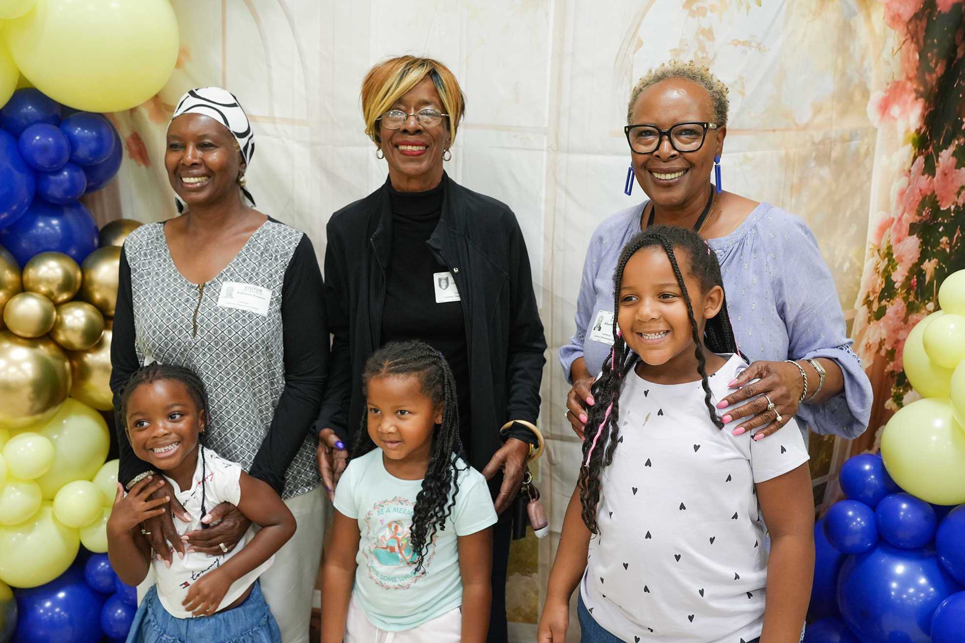 A group of people stands behind balloons. Four adults and three children pose together.