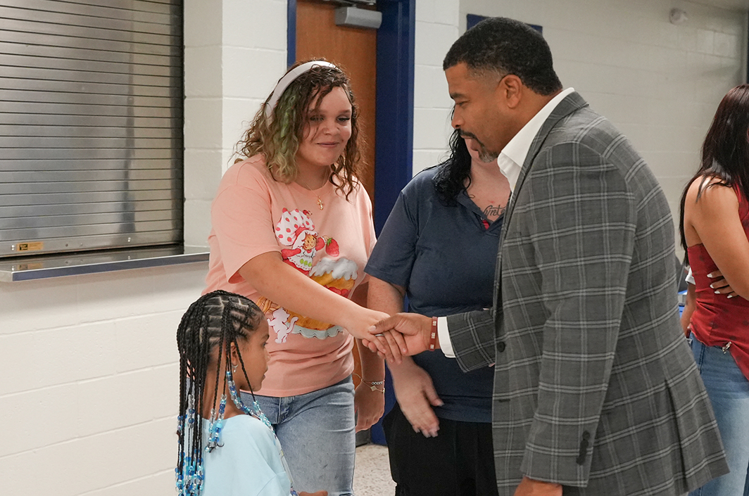 People shake hands in a hallway. A young girl stands next to a woman and a man.