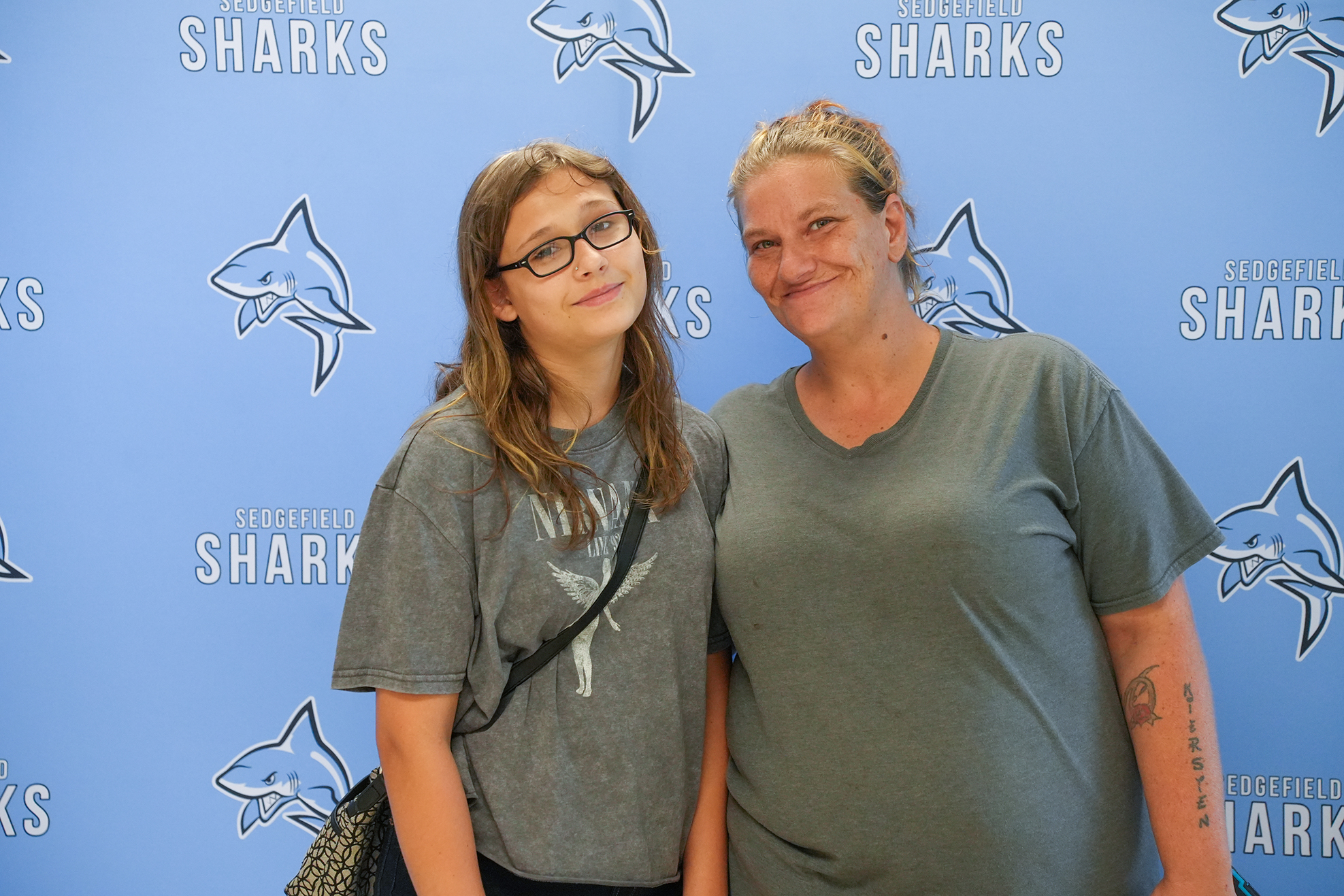 Two women stand smiling in front of a blue wall with the word "Sharks" and shark images.