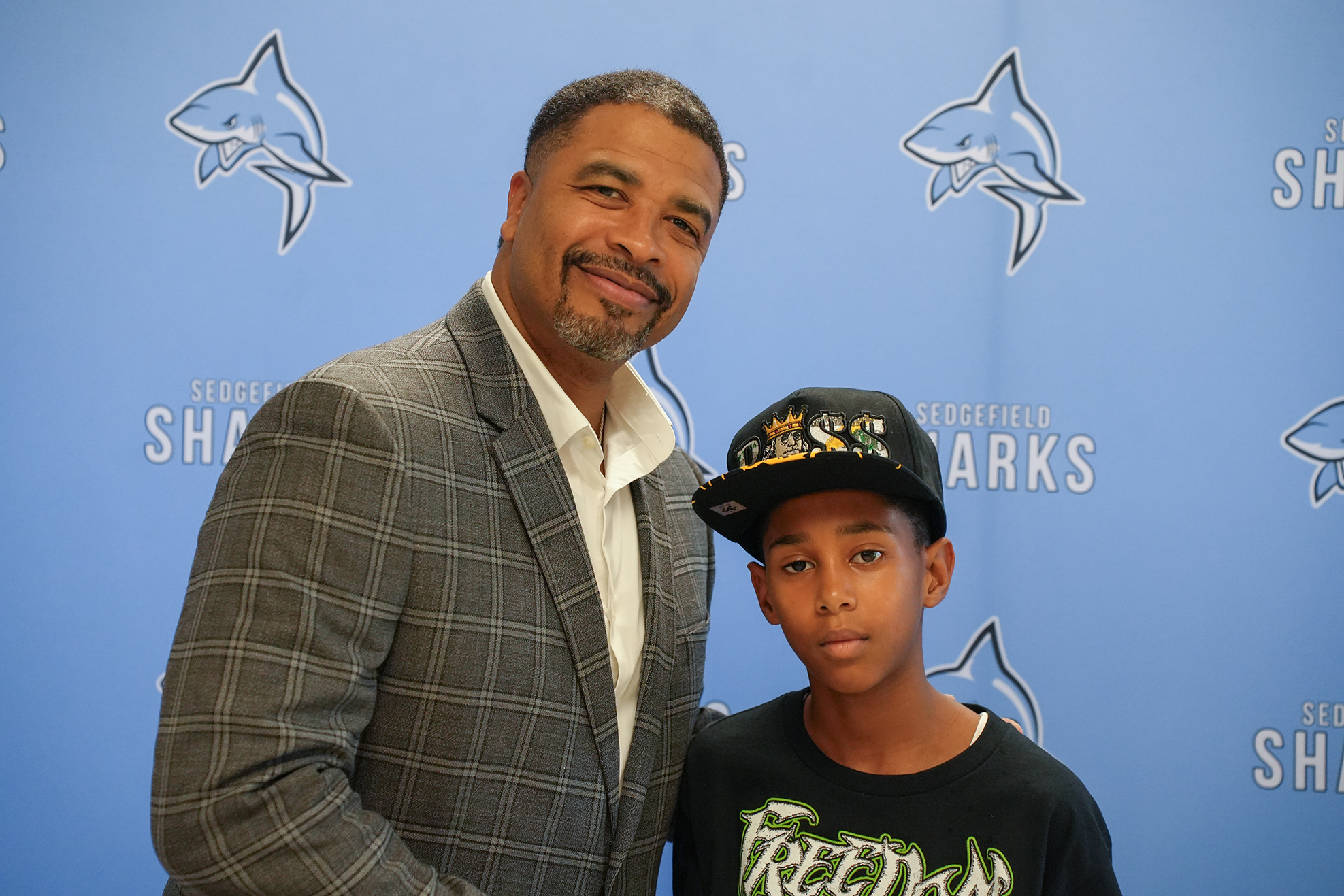 A man and a boy pose in front of a blue wall with large shark images.