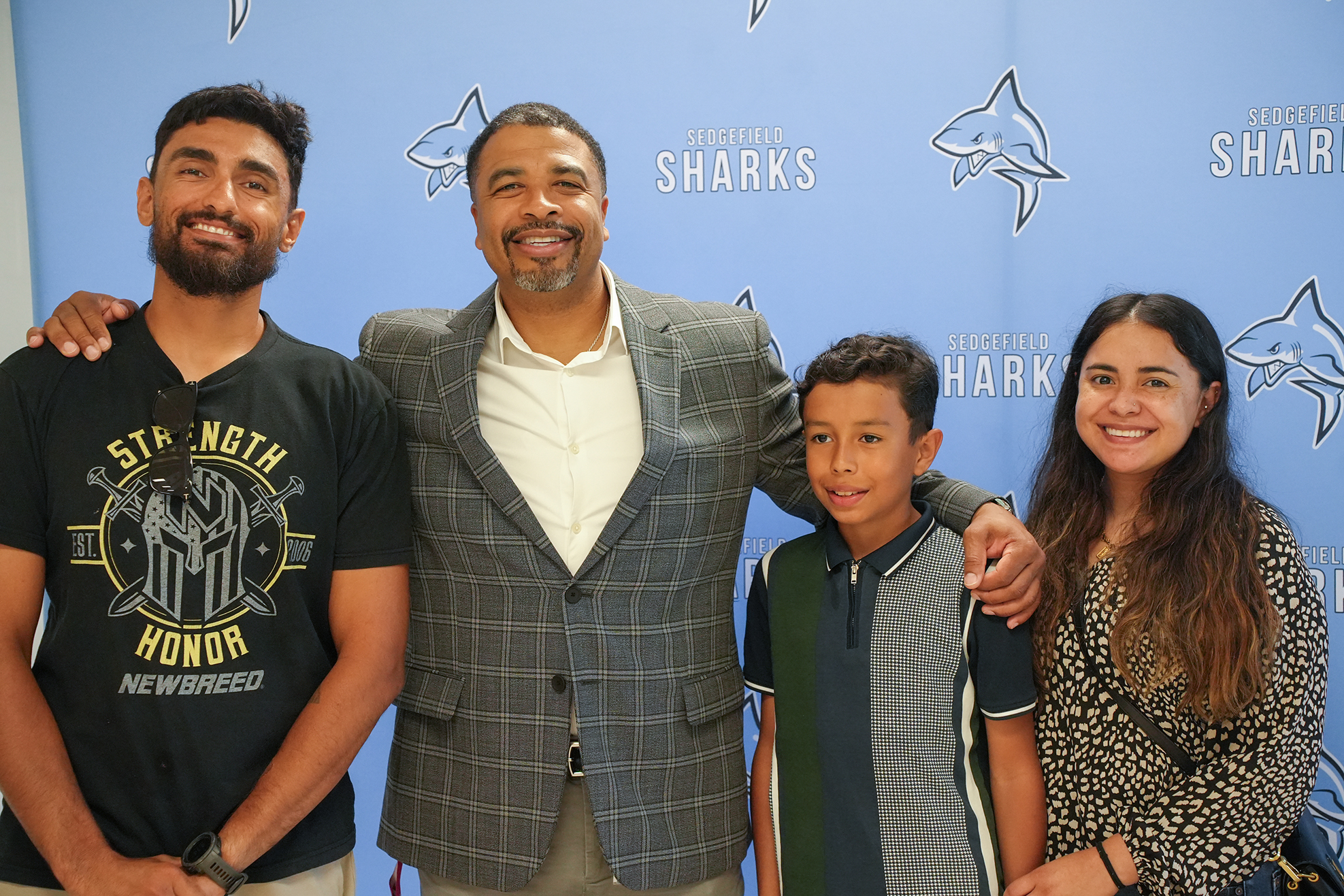 Four individuals pose for a photo in front of a blue backdrop featuring a shark logo.