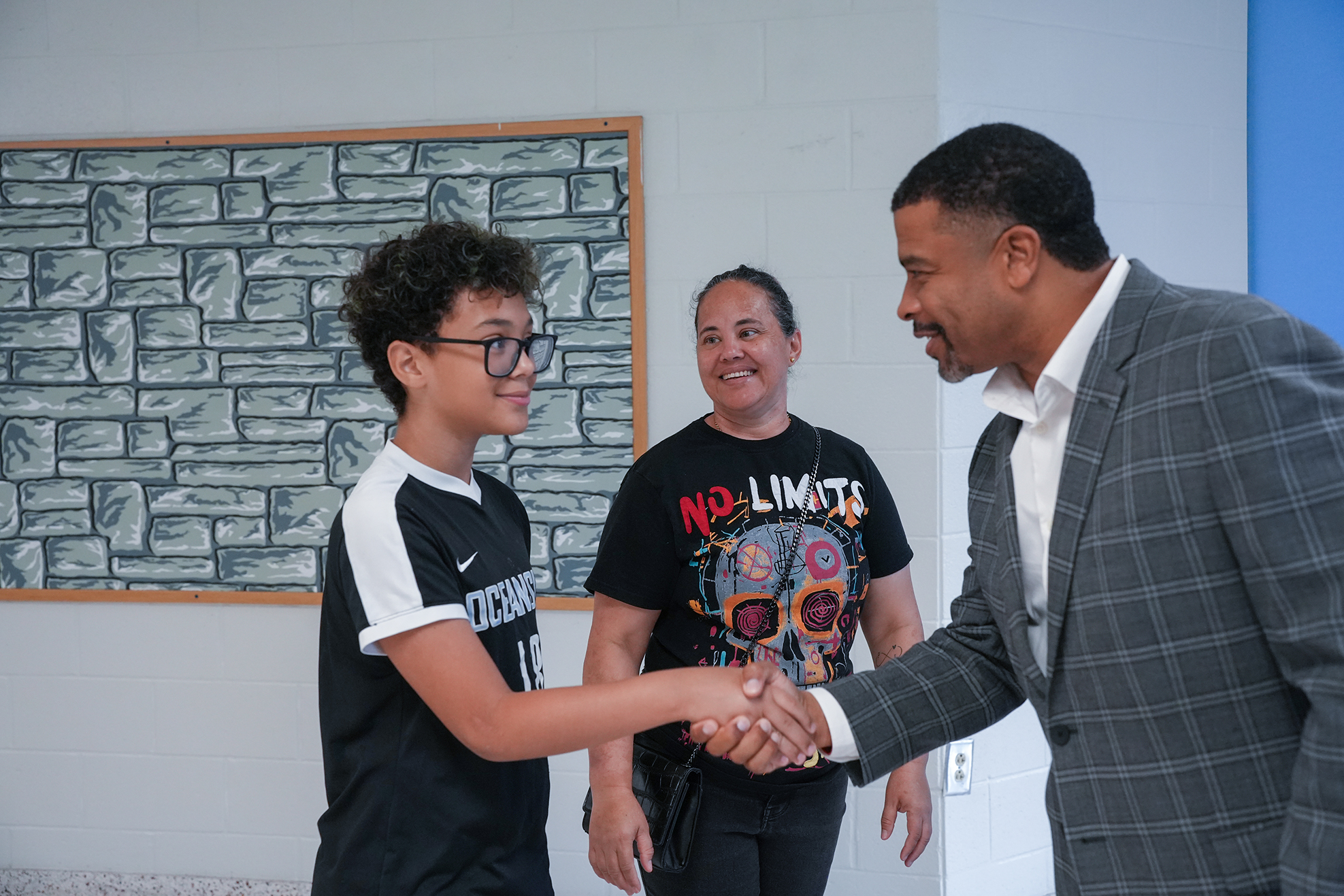 Three individuals, one in a suit and two in casual clothes, are shaking hands in a room.