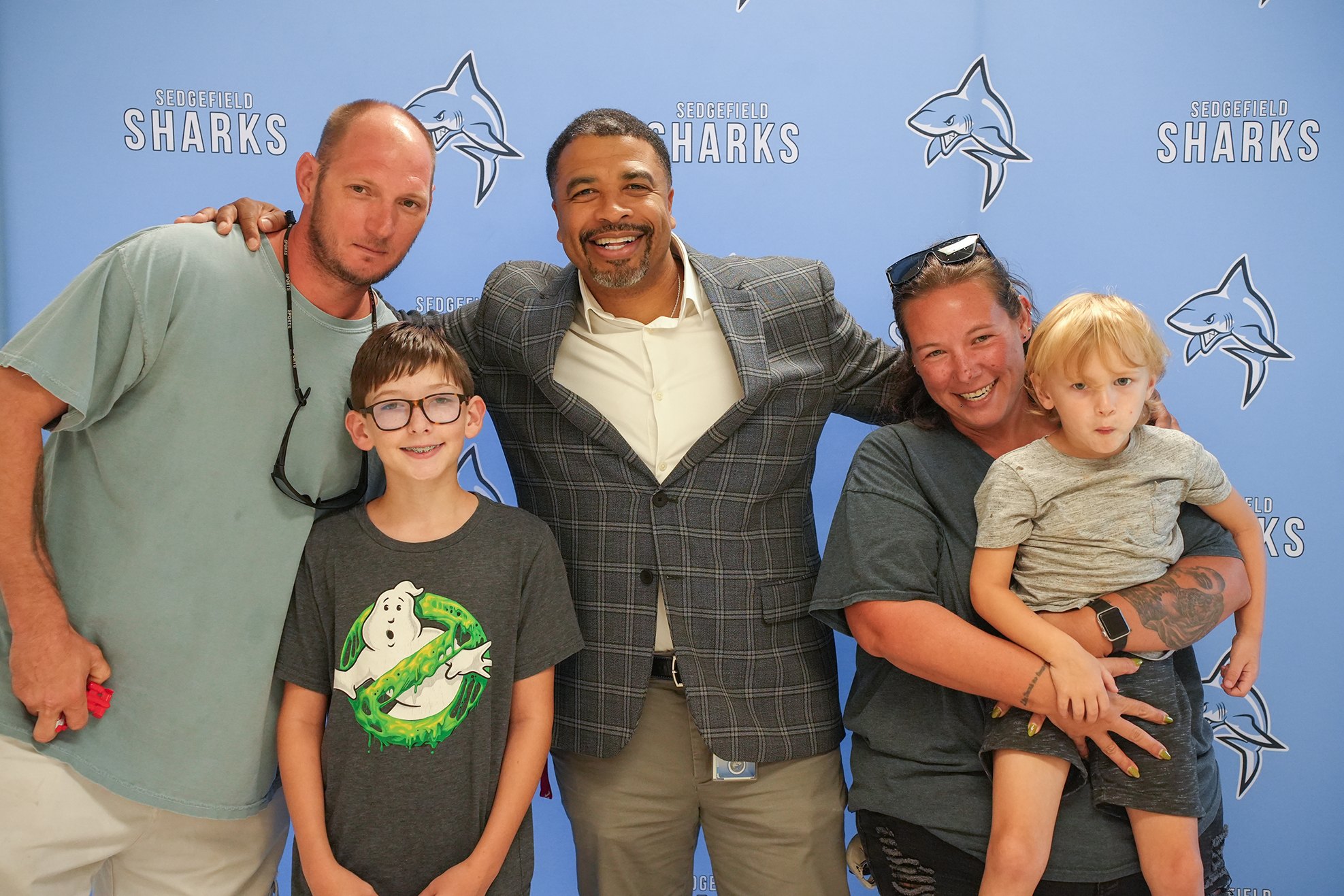 Four individuals, including two children, pose for a photo against a blue backdrop with a sharks logo.