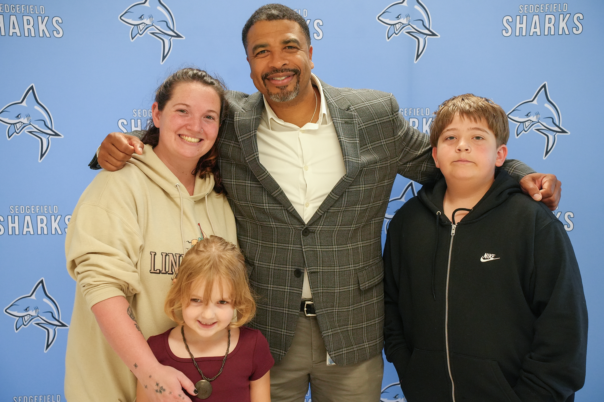 A man and two children pose for a picture with a woman, all standing in front of a blue backdrop.