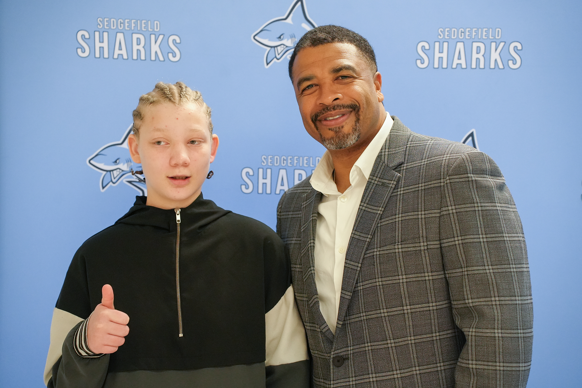 A man and a young boy stand together in front of a wall with a shark logo.