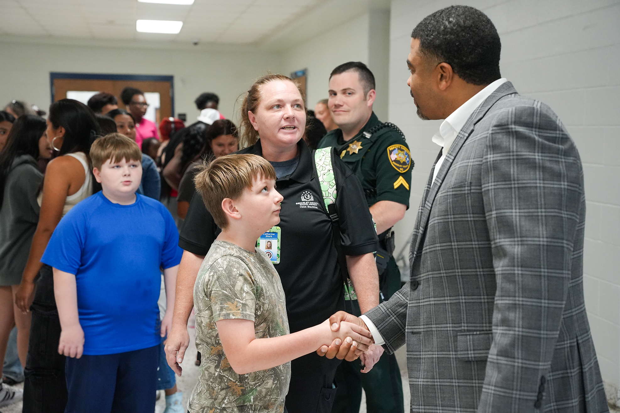 An adult man in a gray suit shakes hands with a young boy in a camo shirt.