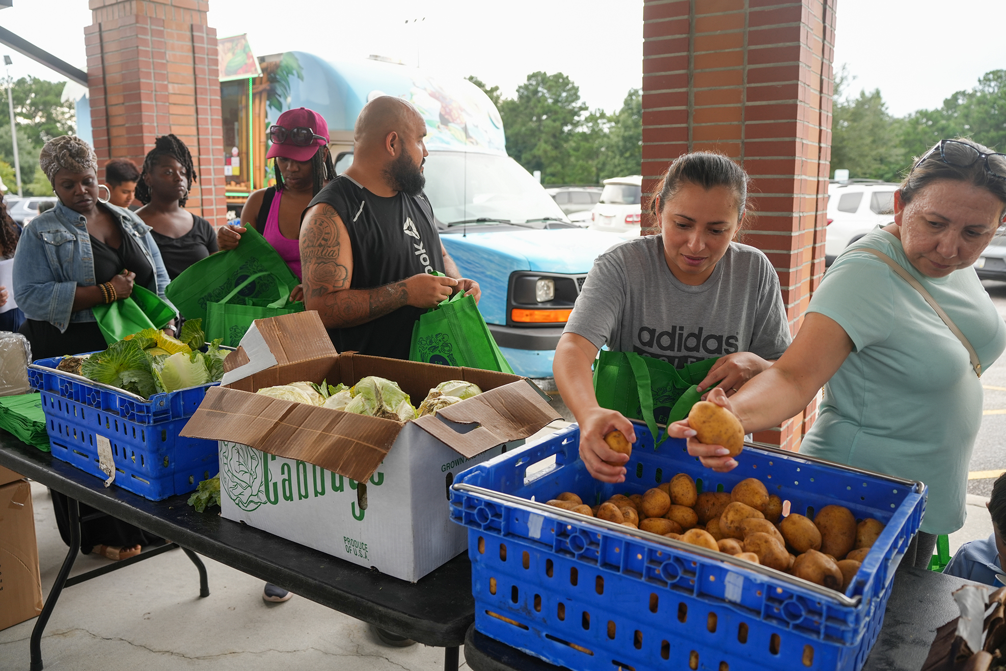Group of people in a parking lot preparing food boxes with produce. One holds a potato.