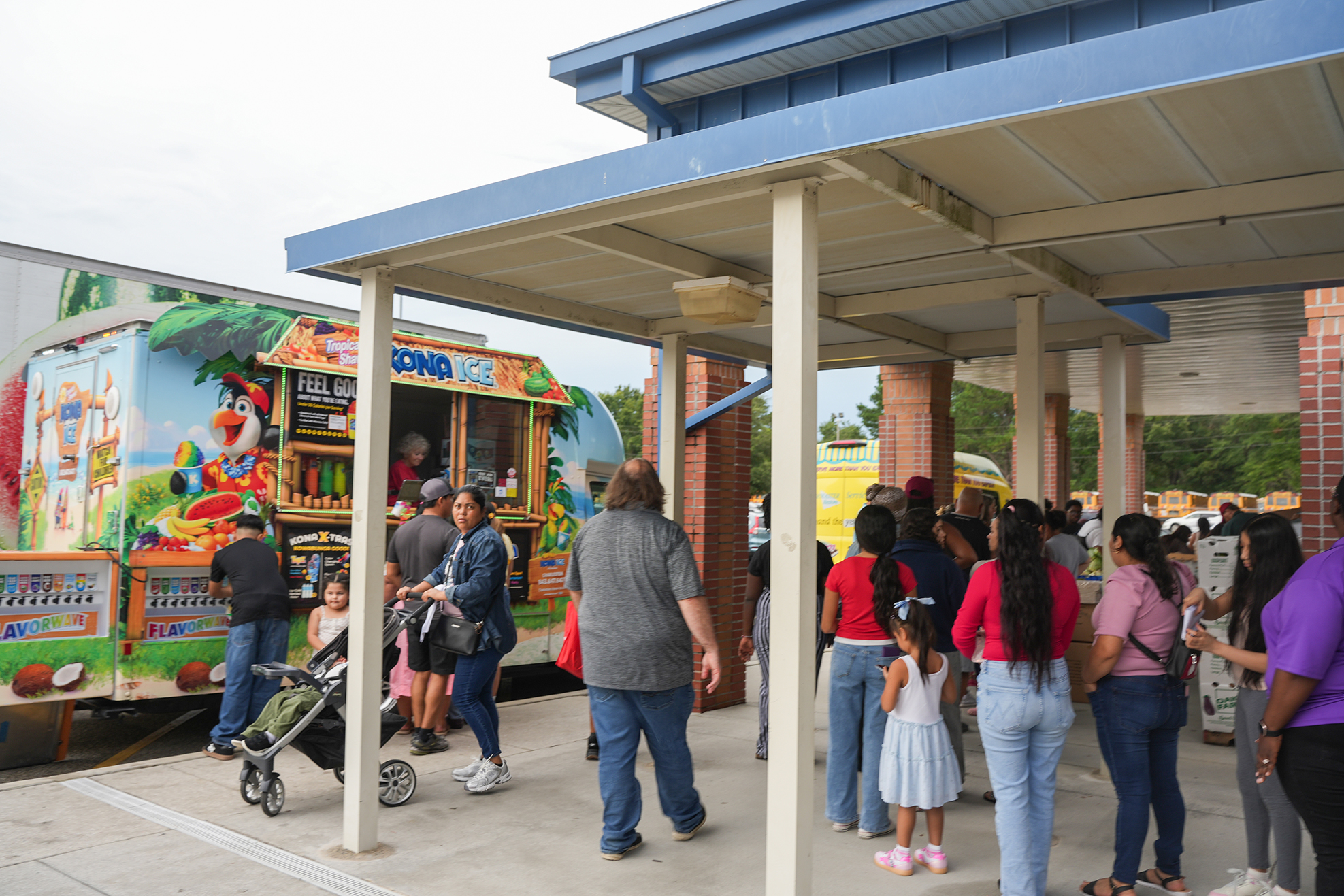 A group of people wait under a shelter, with a food truck in the background.