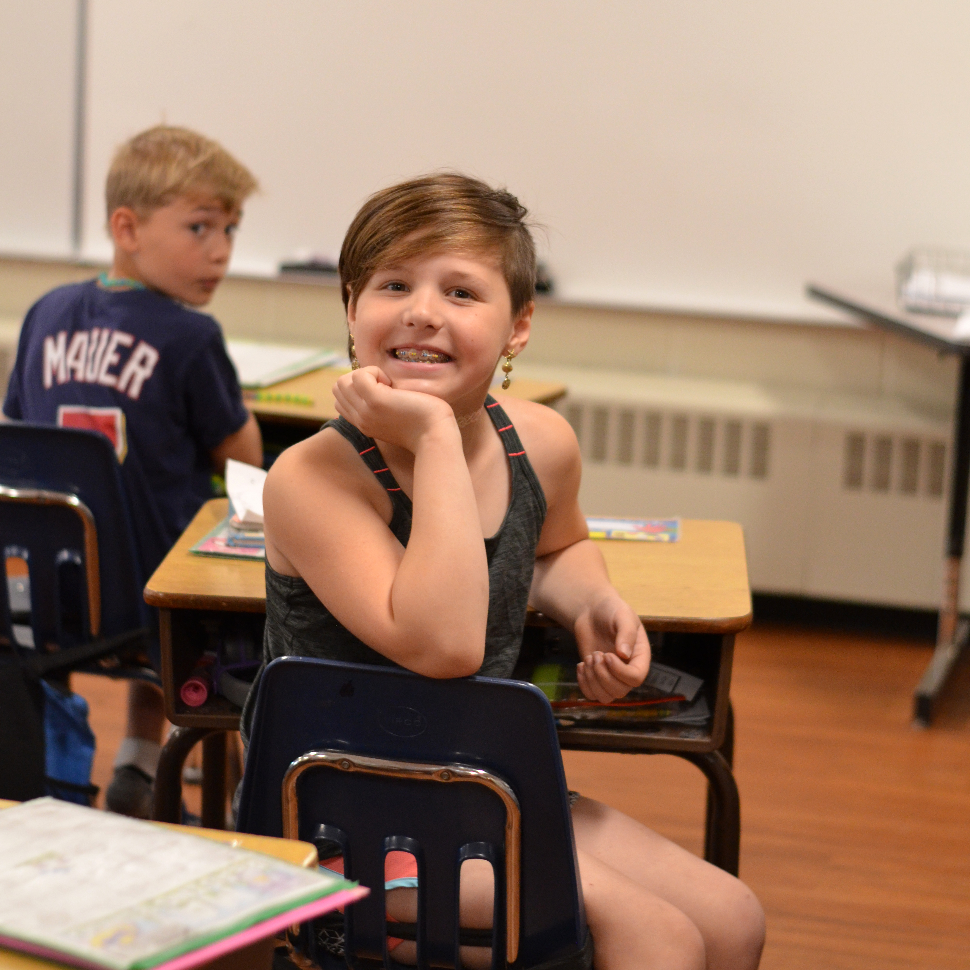 A student with short hair sitting at her desk, smiling brightly at the camera