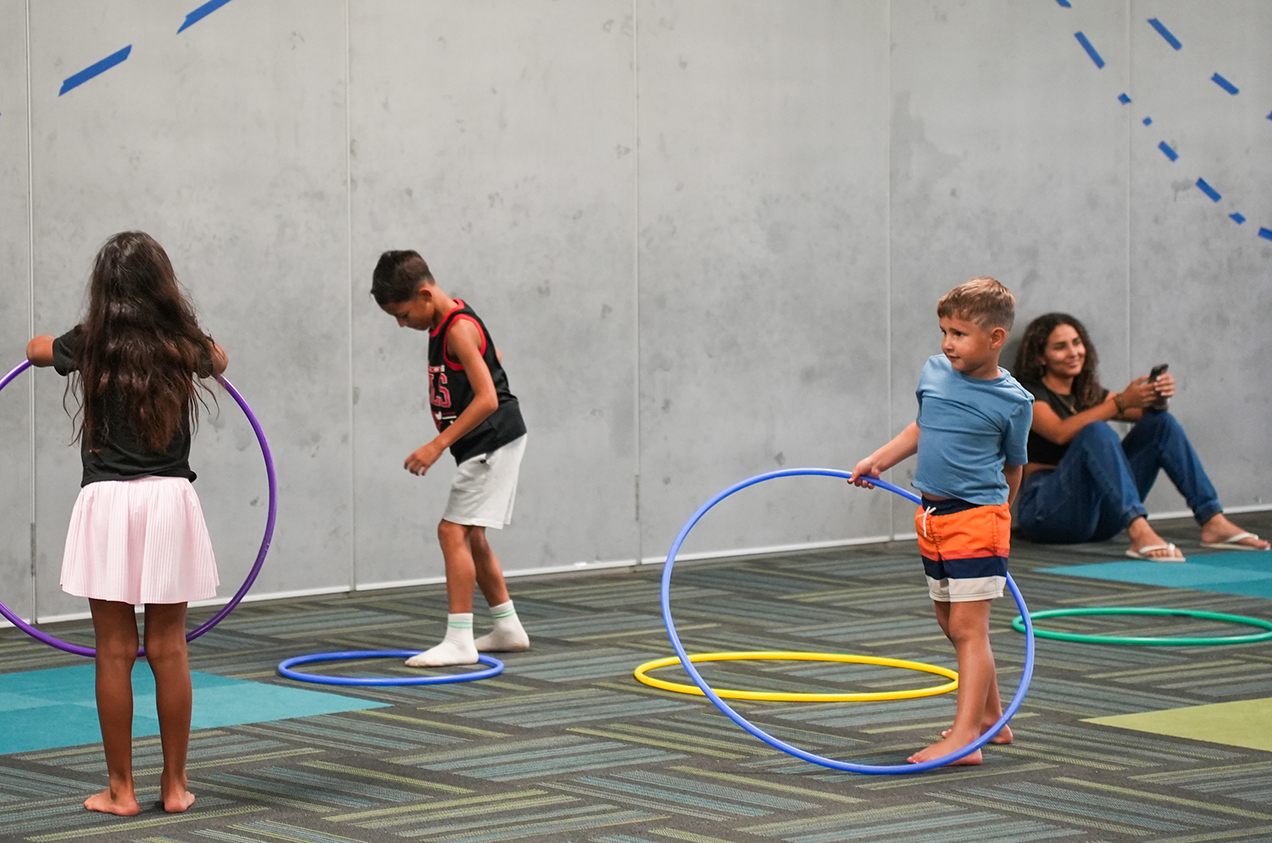 Four children are playing with hula hoops in a room. Two are standing while two are sitting.