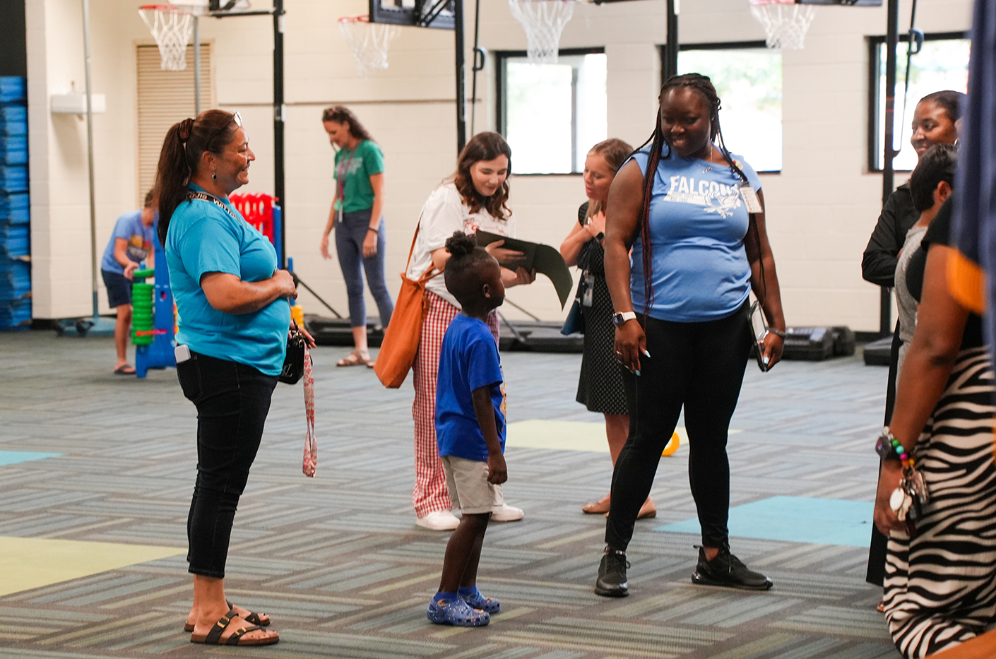 Adults and children in a gym, including a child wearing a blue shirt and shorts.