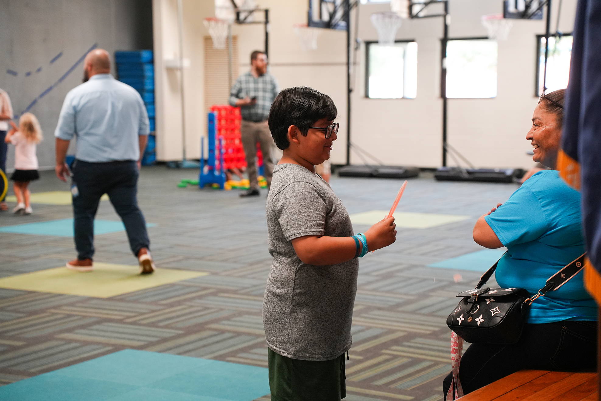 People are in a gym with exercise equipment in the background. One person holds an orange object.