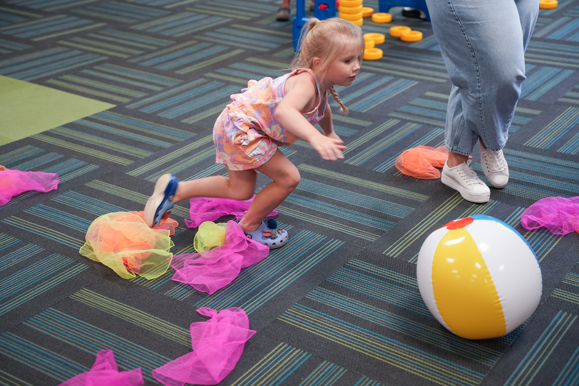 A young child plays with a beach ball and fabric streamers on a carpeted floor.