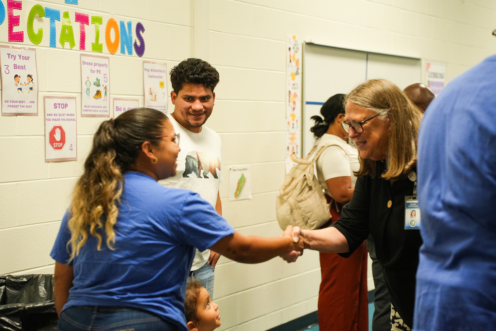 Several people in a room with educational posters on the wall, two adults shaking hands.