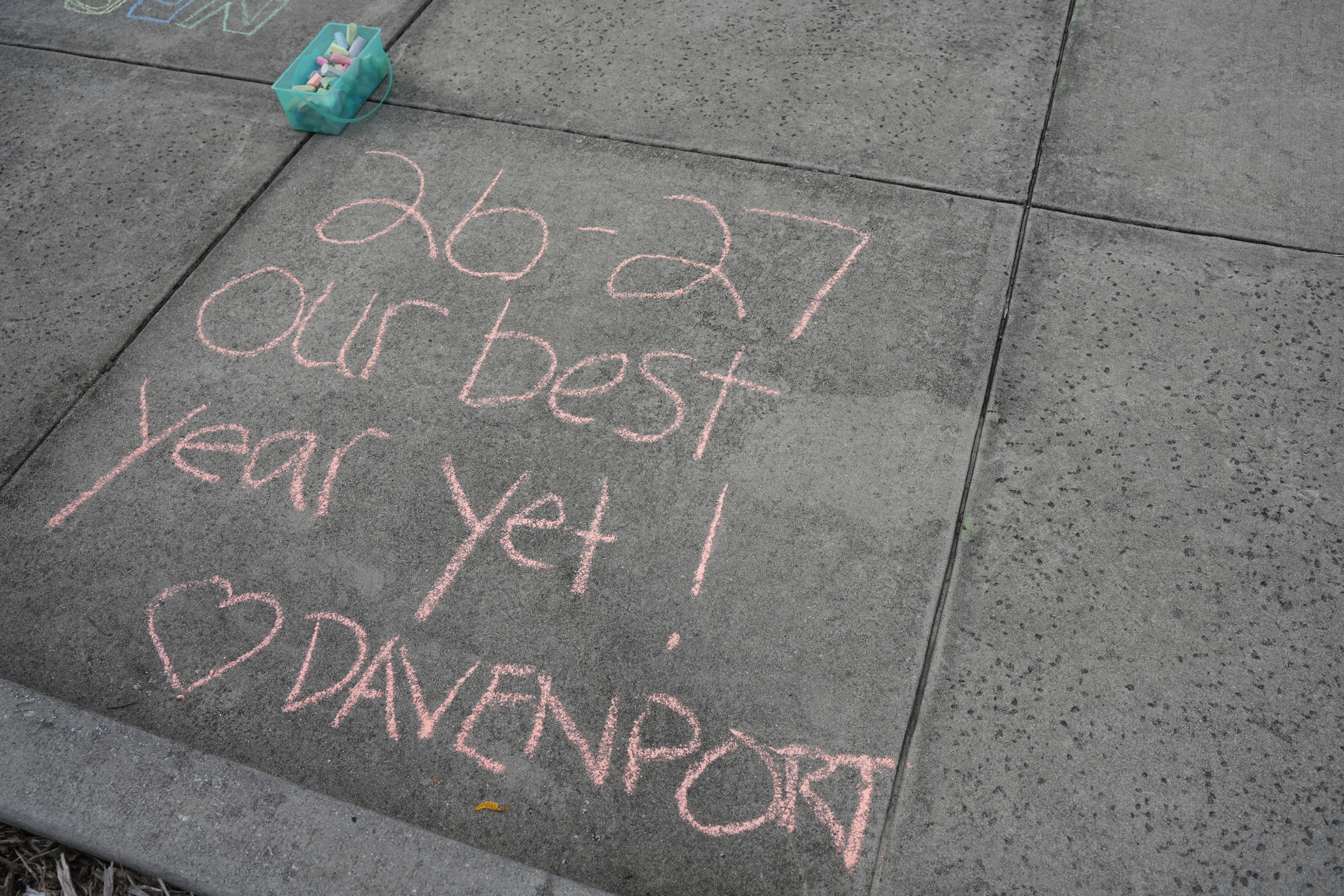 Sidewalk with chalk message reading "26-27 our best year yet! I Davenport", with a small object on the left.