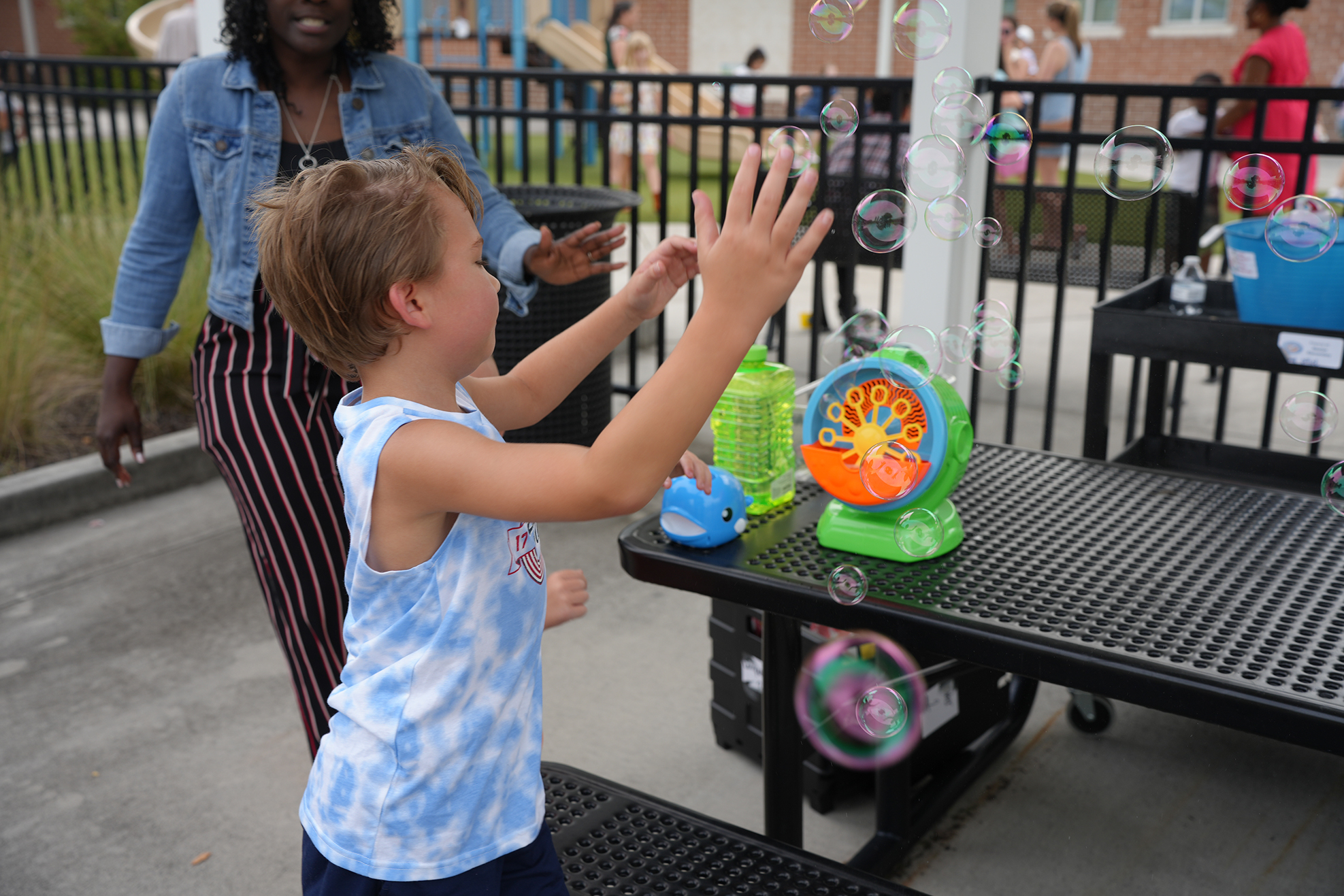 A young child reaches up with arms outstretched to make bubbles using a bubble machine.