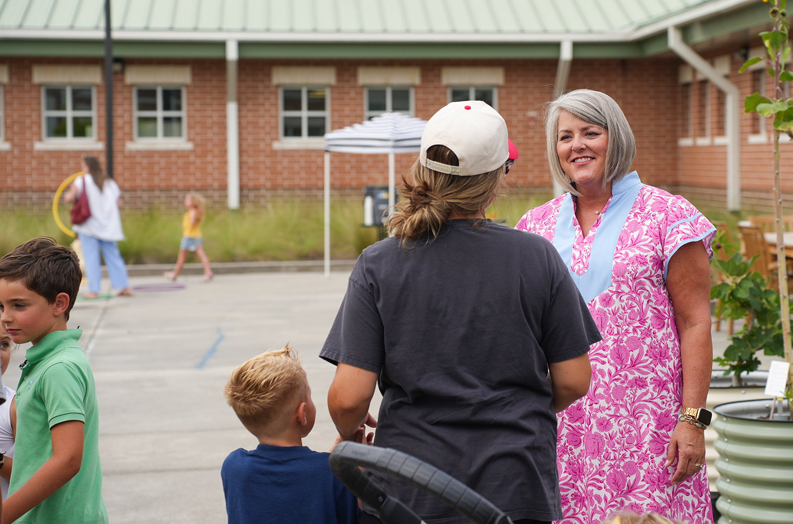 Two women and three children in a parking lot, one woman in a white cap and another in pink.