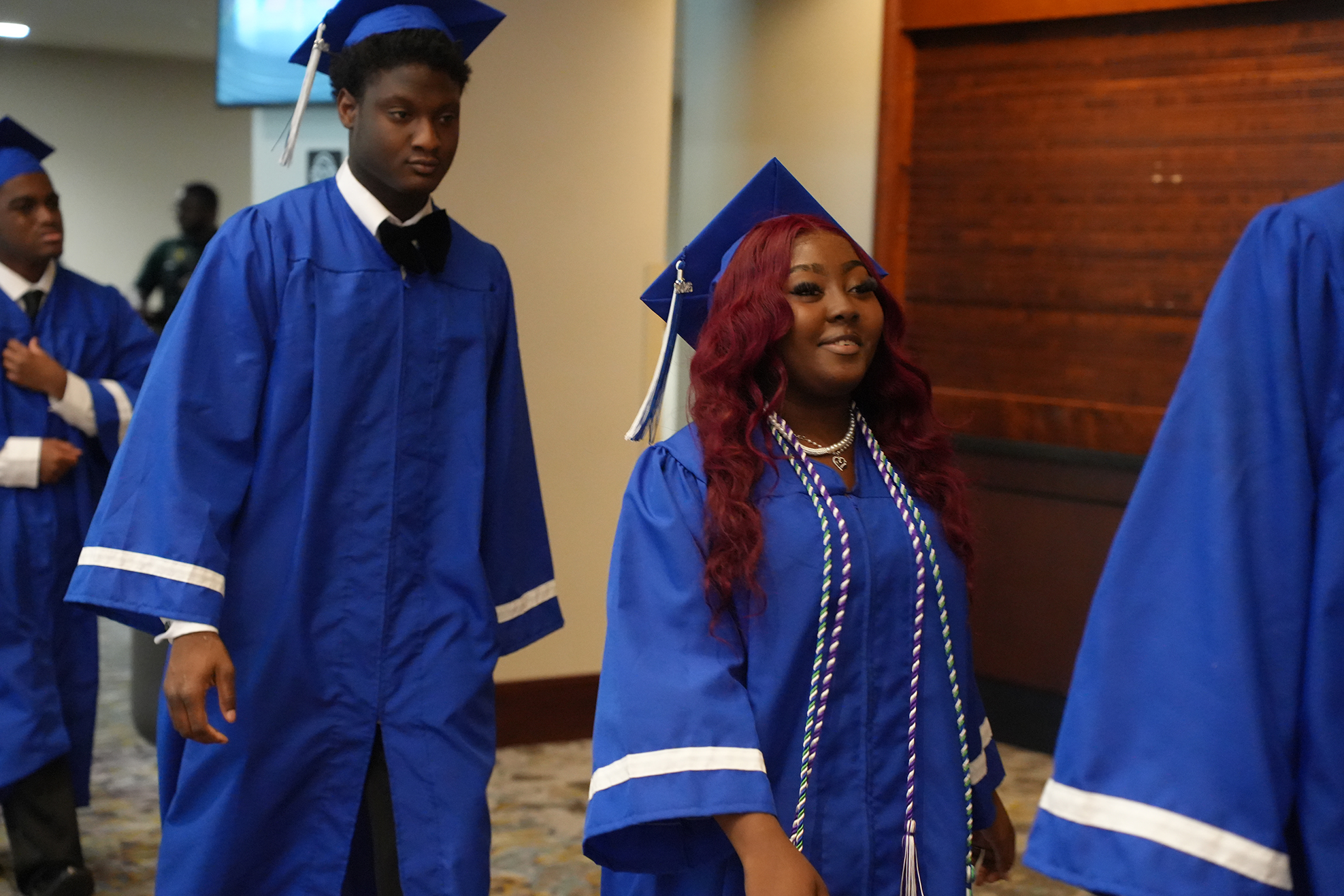 Several people in blue gowns walk down a corridor. A man and woman are in the front.