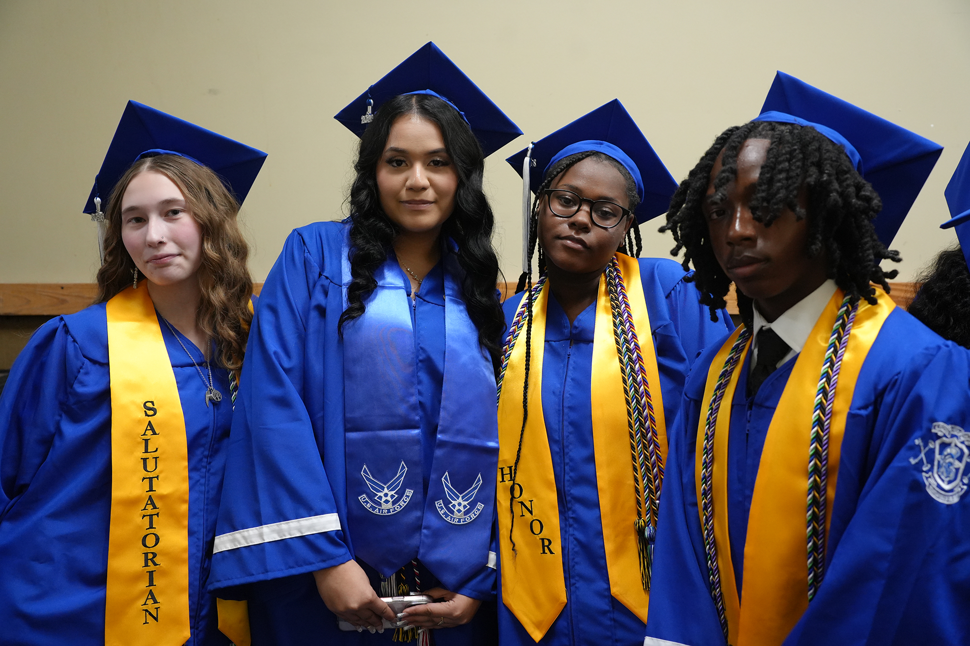Four people in blue and yellow graduation gowns and caps, smiling and posing for a photo.
