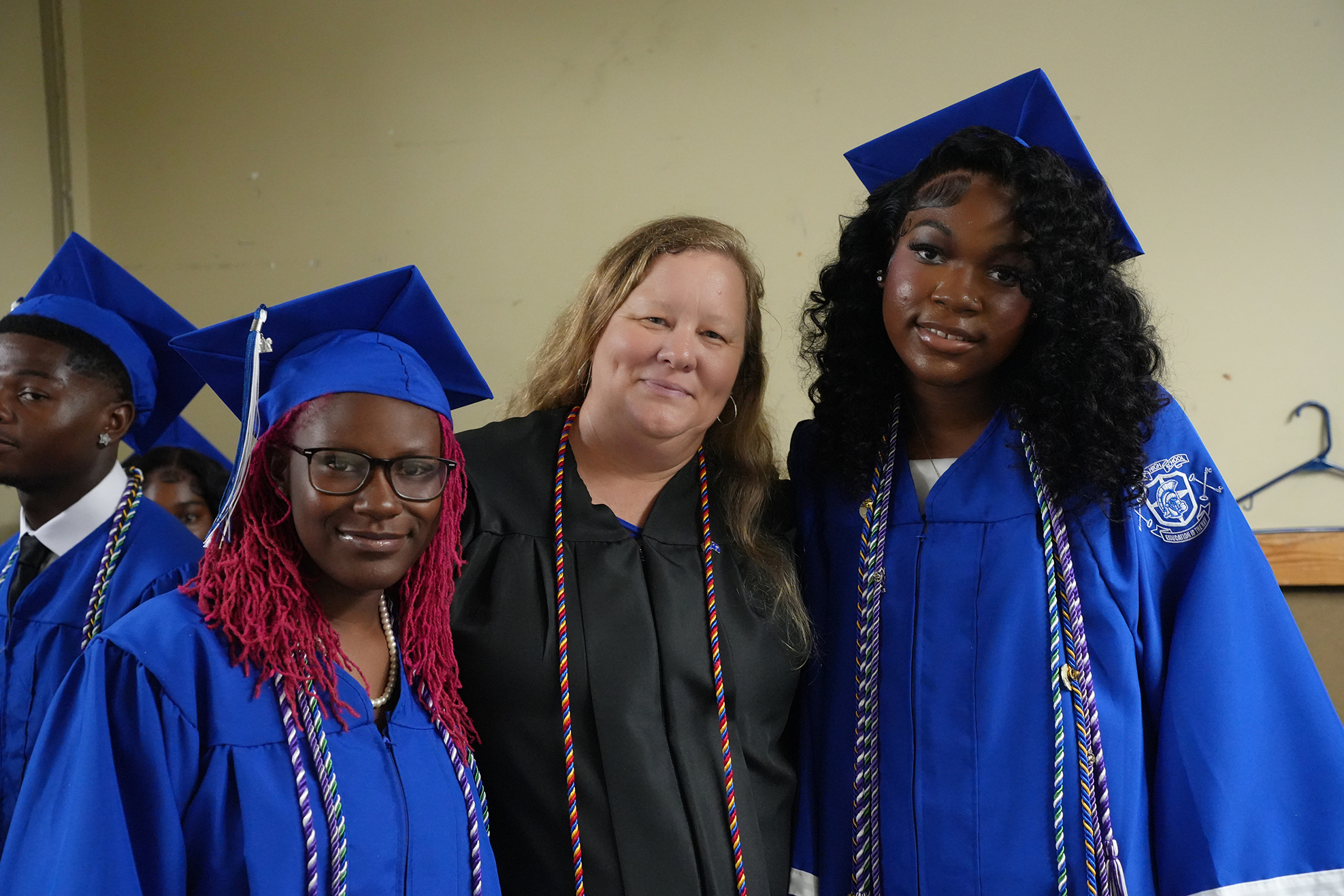 A group of students in blue graduation gowns pose for a picture. One wears glasses and has red hair.