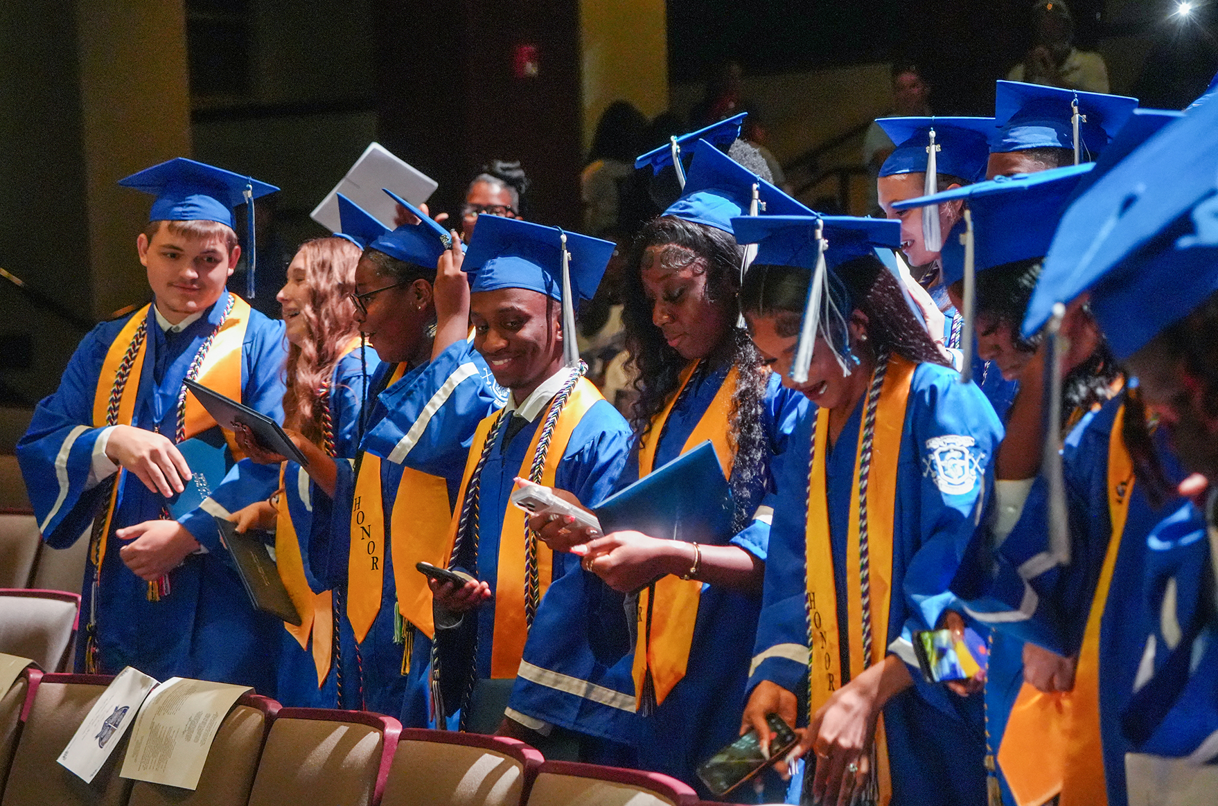 A group of young adults dressed in blue and gold gowns and hats, standing in a row at an event.