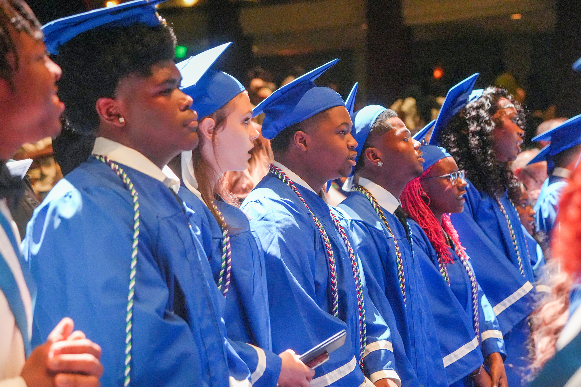 A group of students in blue gowns and caps are lined up, possibly for a graduation ceremony.
